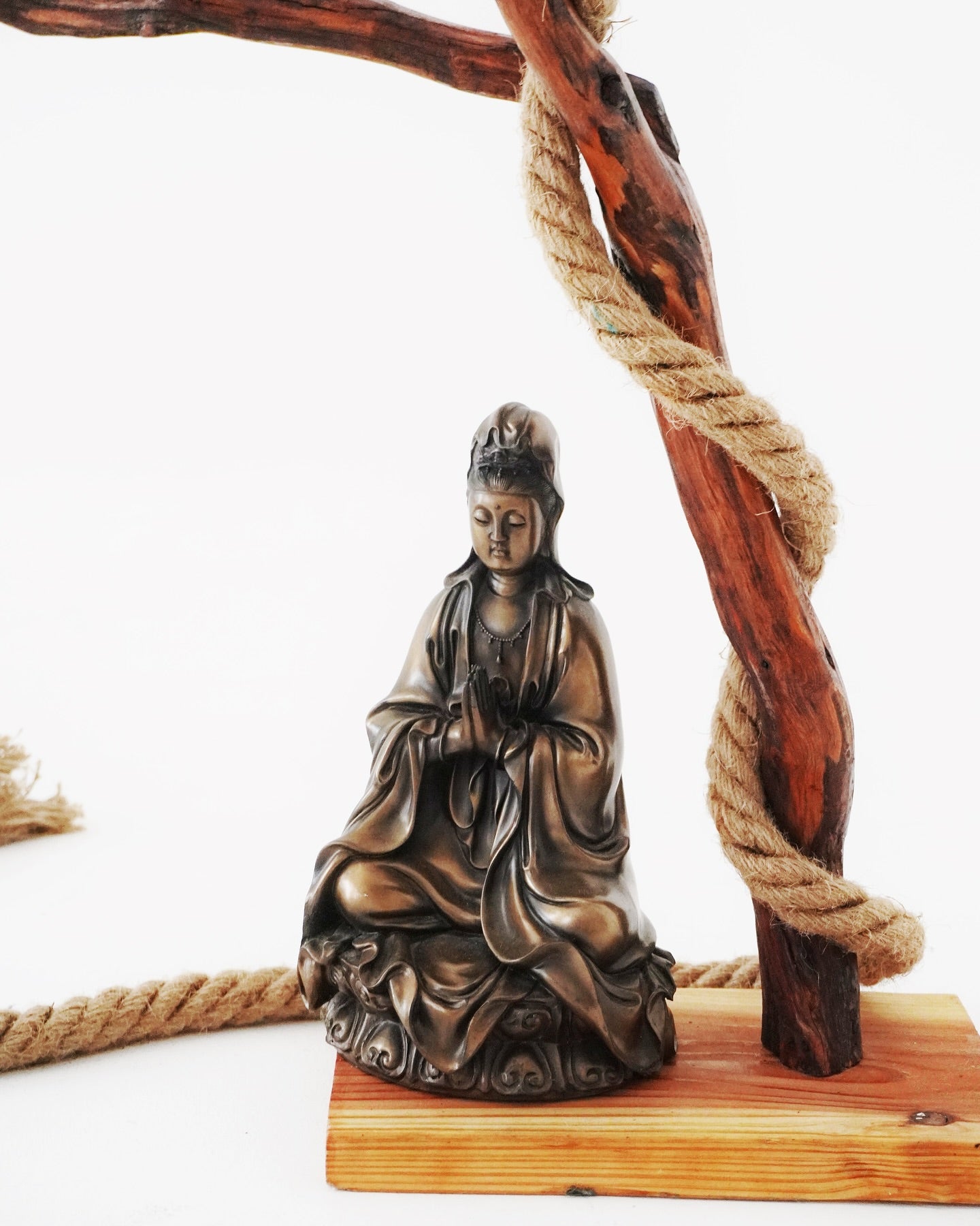 Bronze statue of a seated figure on a wooden base with rope and wood piece