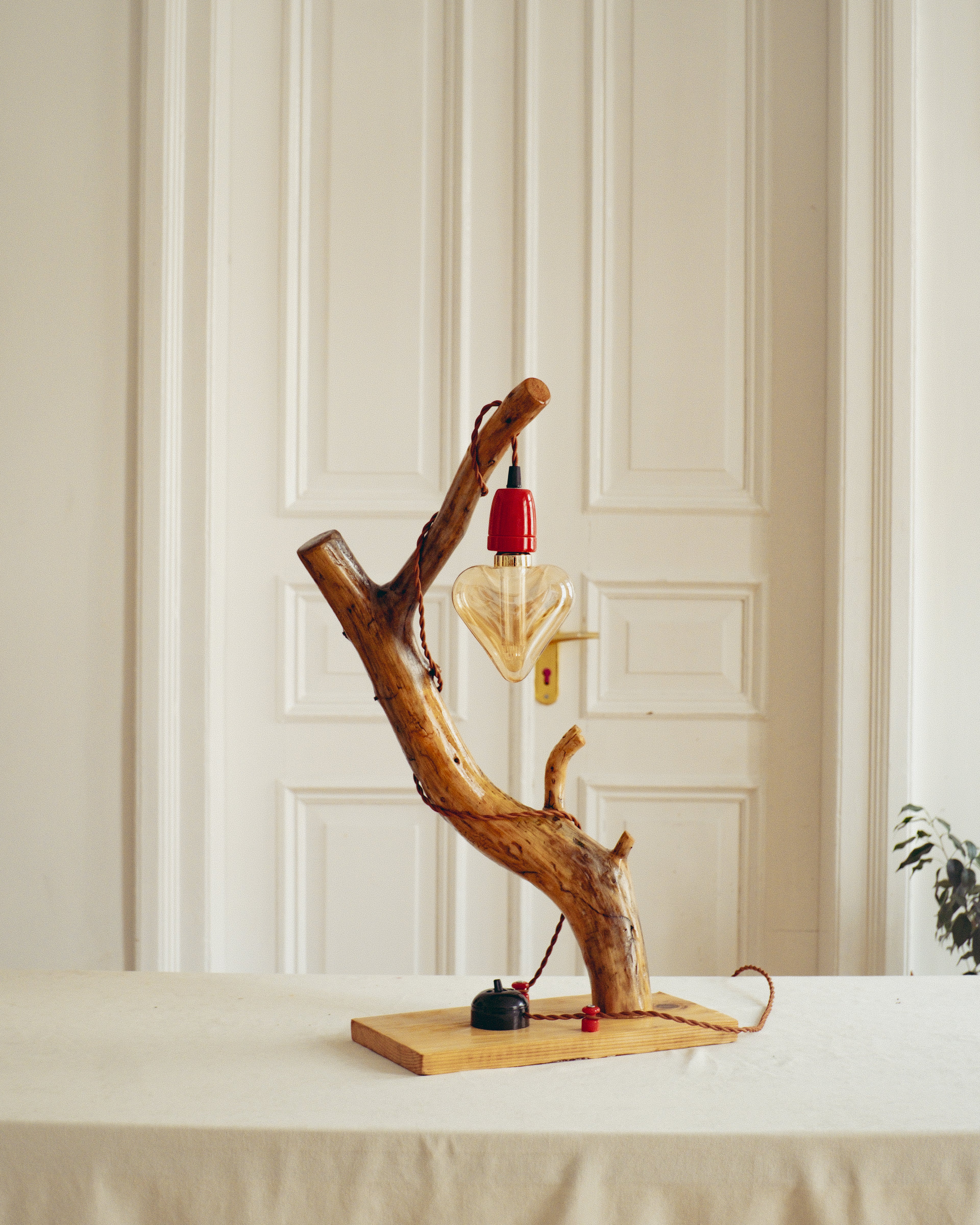 handmade lamp with a red light bulb on a white surface against a beige paneled wall.