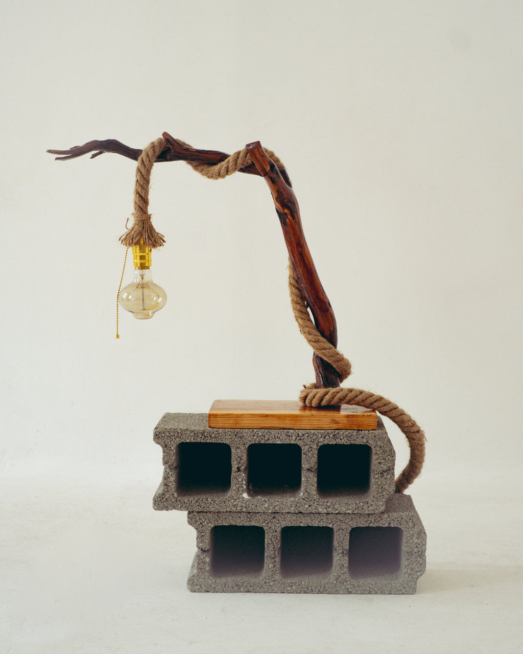 Decorative lamp with a rope and light bulb on a concrete block base against a white background