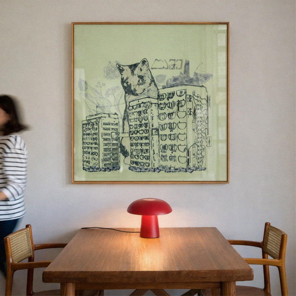 Room interior with a wooden table, red lamp, and framed artwork of a cat on a building.