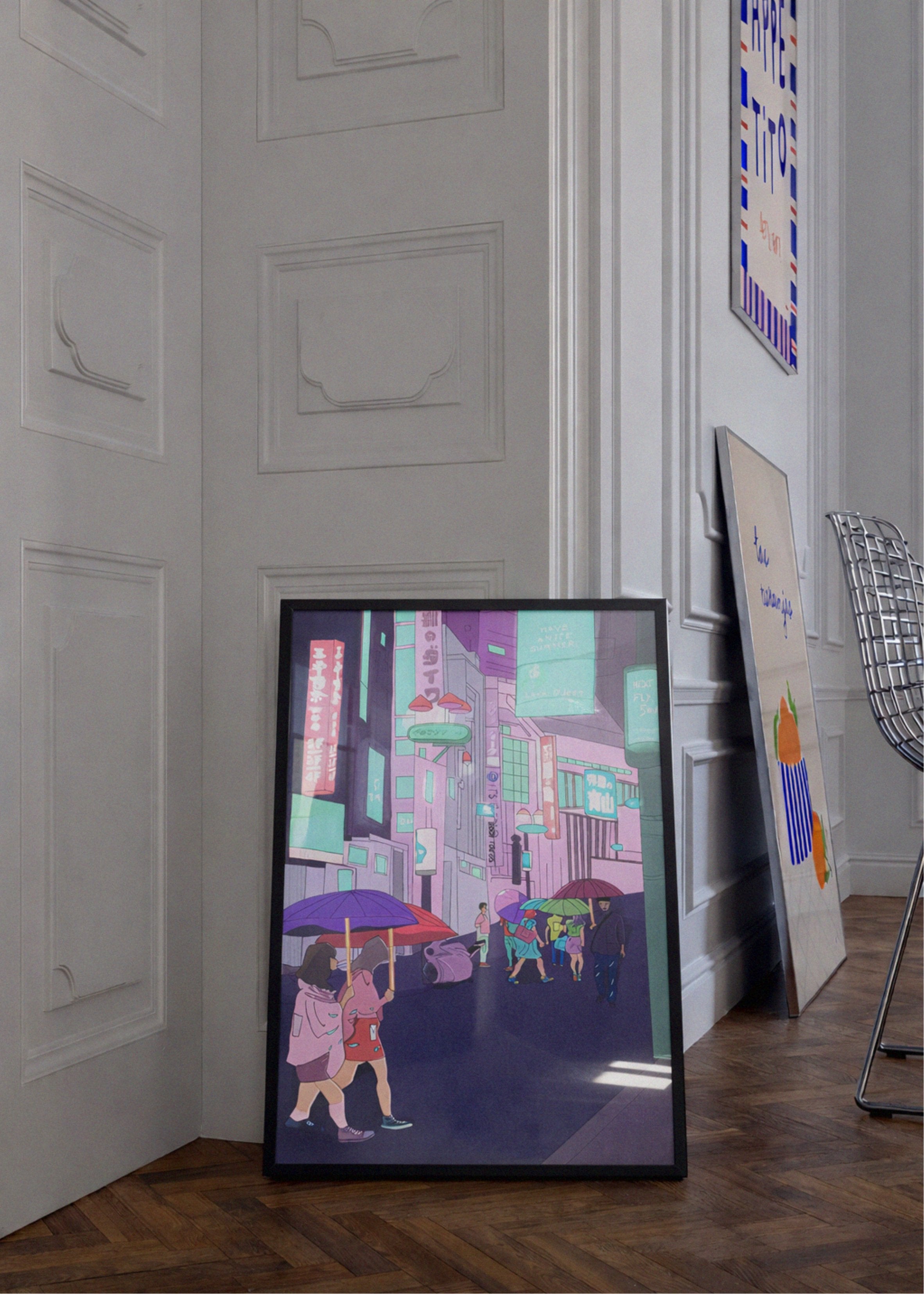 Framed artwork of a cityscape with people holding umbrellas in a room with white paneled walls.
