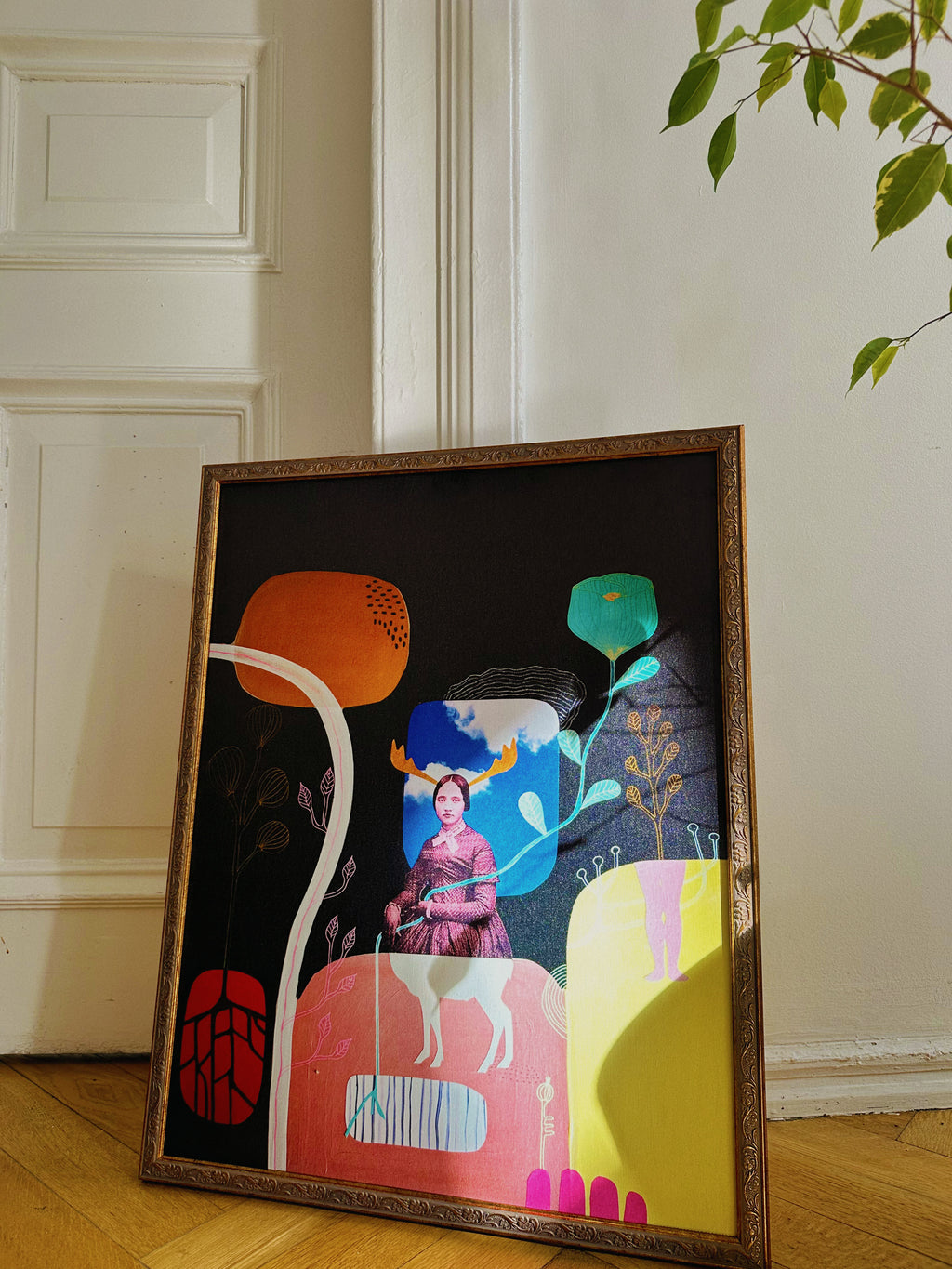 A framed poster featuring a colorful and abstract composition with human-like figures and geometric shapes, leaning against a wall on a wooden floor.