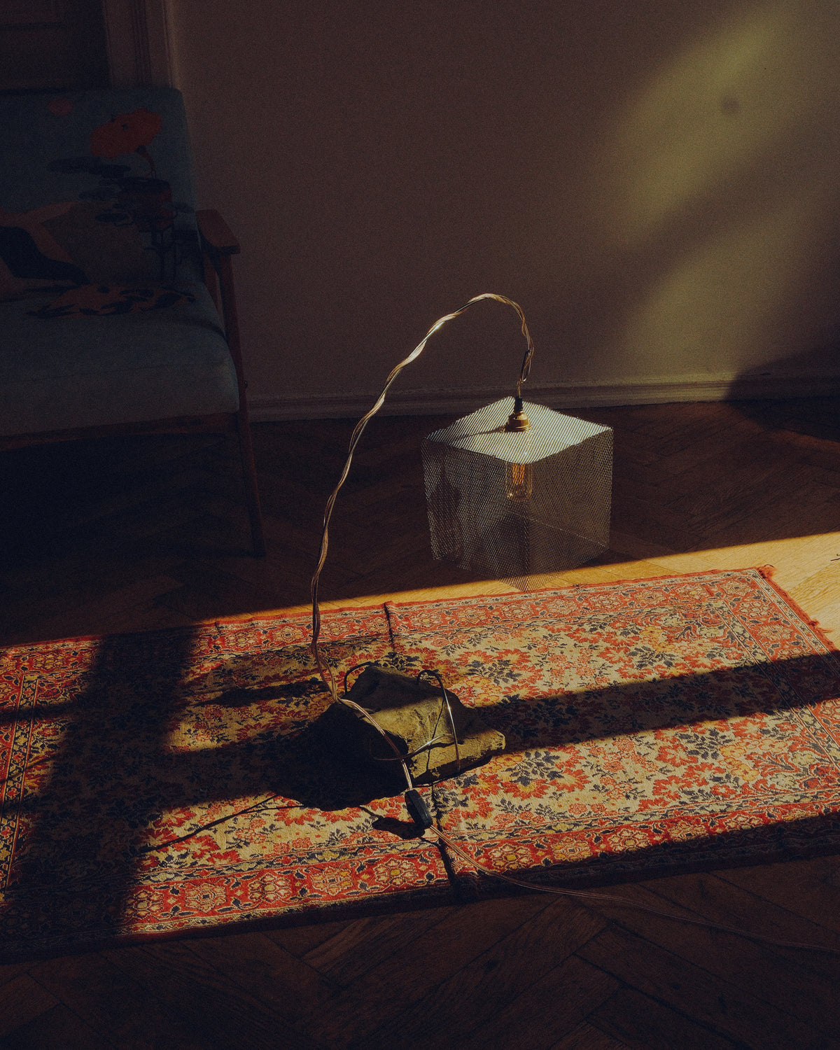 Lifestyle view of the handmade “Loop” lamp, featuring a natural stone base, curved metal structure and suspended mesh shade in a warm interior setting.