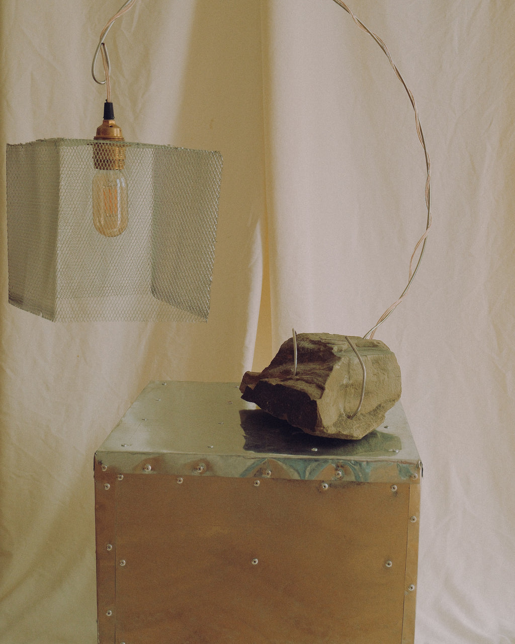 Handmade sculptural lamp “Loop” crafted from natural stone and metal, featuring a curved metal structure and suspended mesh shade.