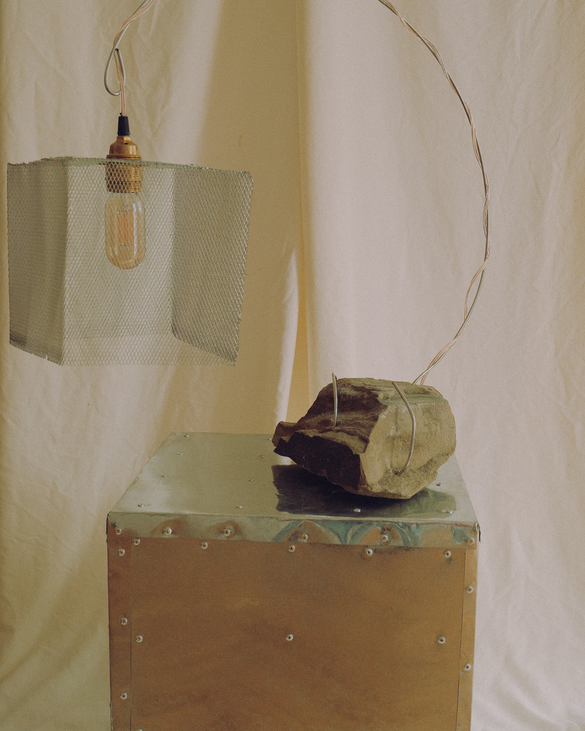 Handmade sculptural lamp “Loop” crafted from natural stone and metal, featuring a curved metal structure and suspended mesh shade.