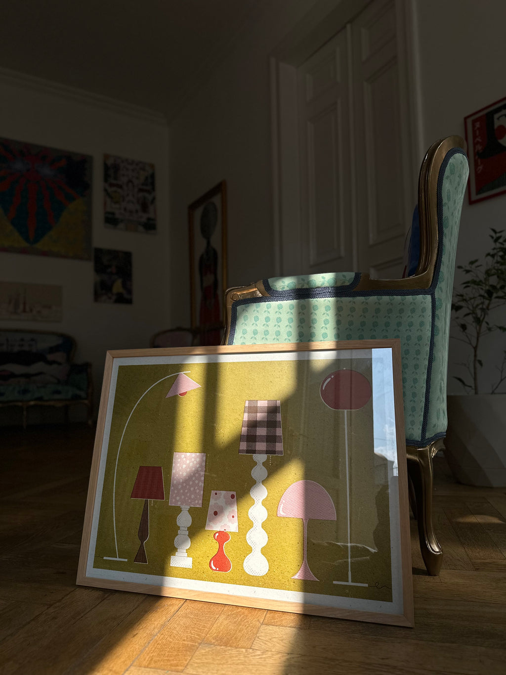 Poster “Mid Century Lamps” by Julia Leister framed and placed in sunlight on wooden floor