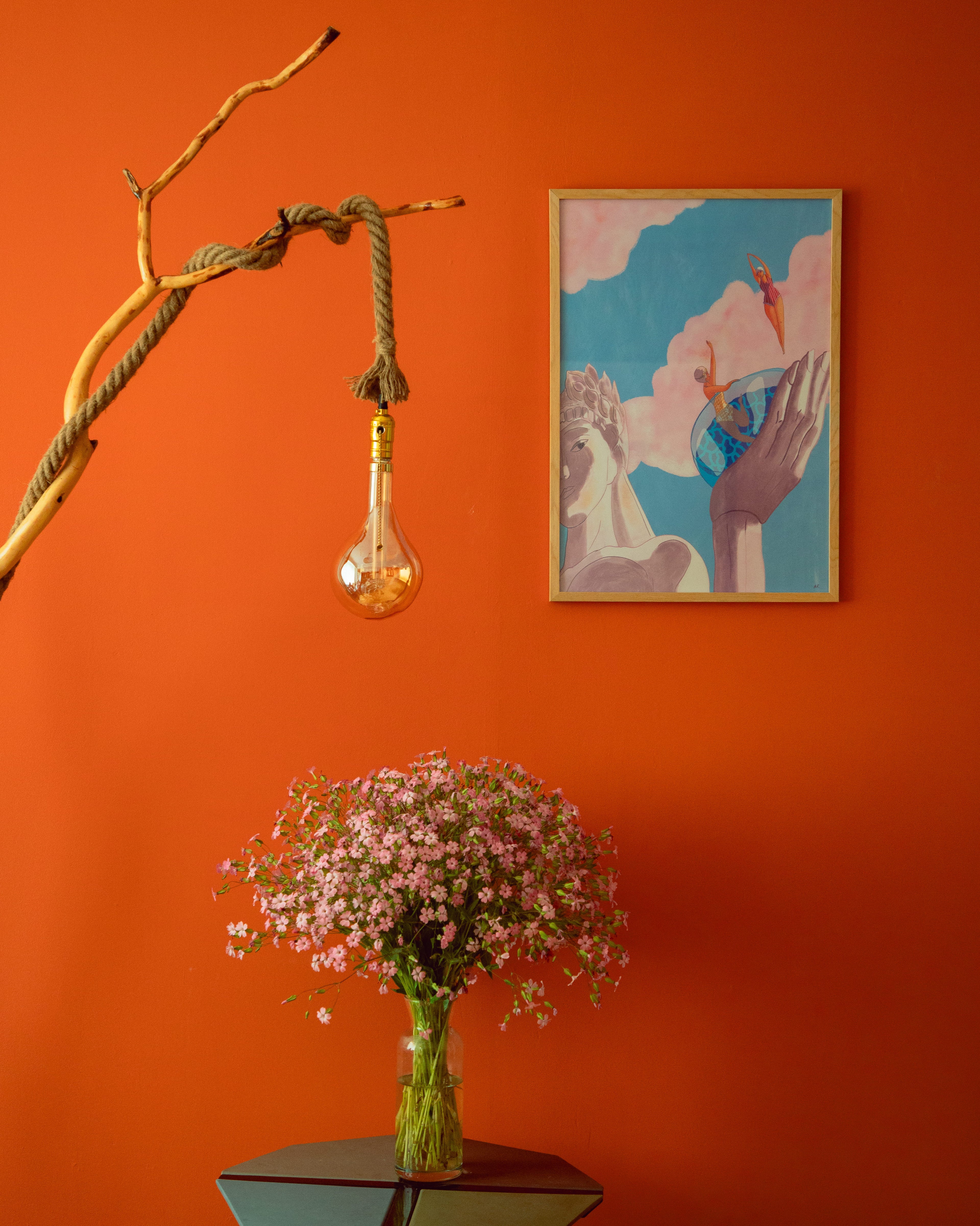 Decorative setup with a light bulb, flowers, and framed artwork on an orange wall.