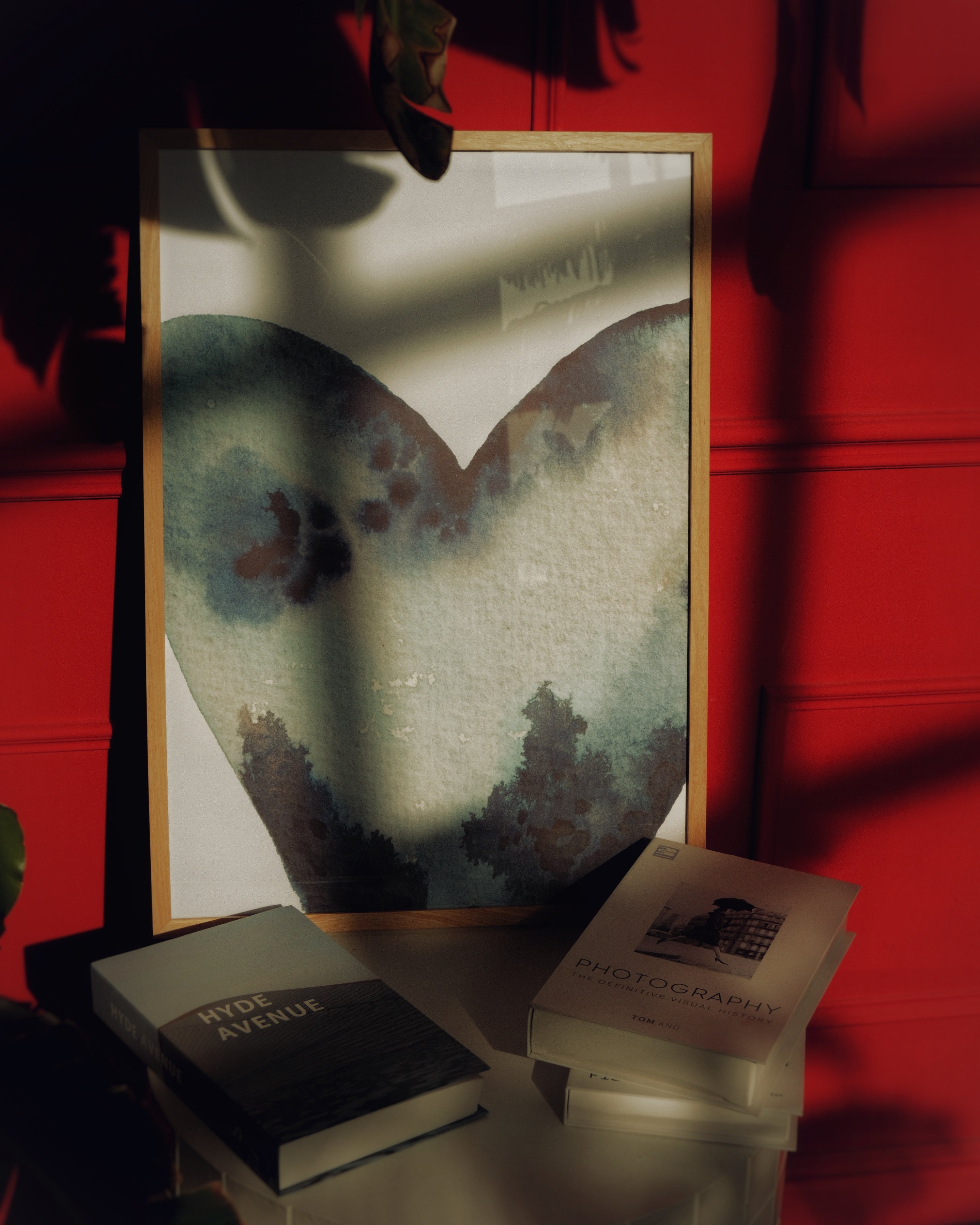 Framed artwork on a table with books against a red wall