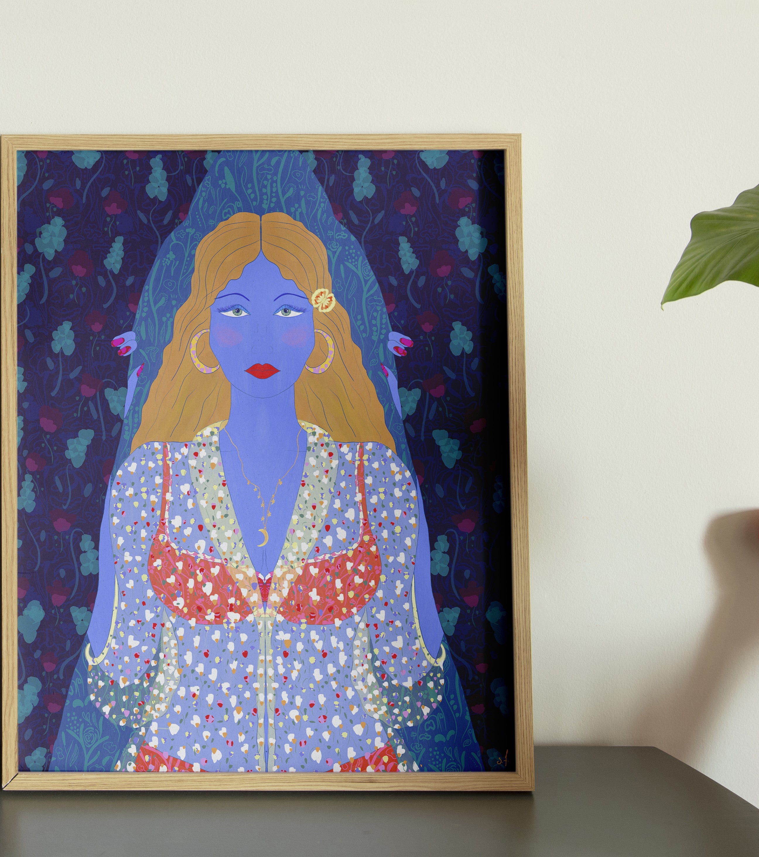 A framed poster of an illustration depicting a character with blue skin, dressed in a multicolored outfit, placed on a floor next to a chair, with natural light falling on it.