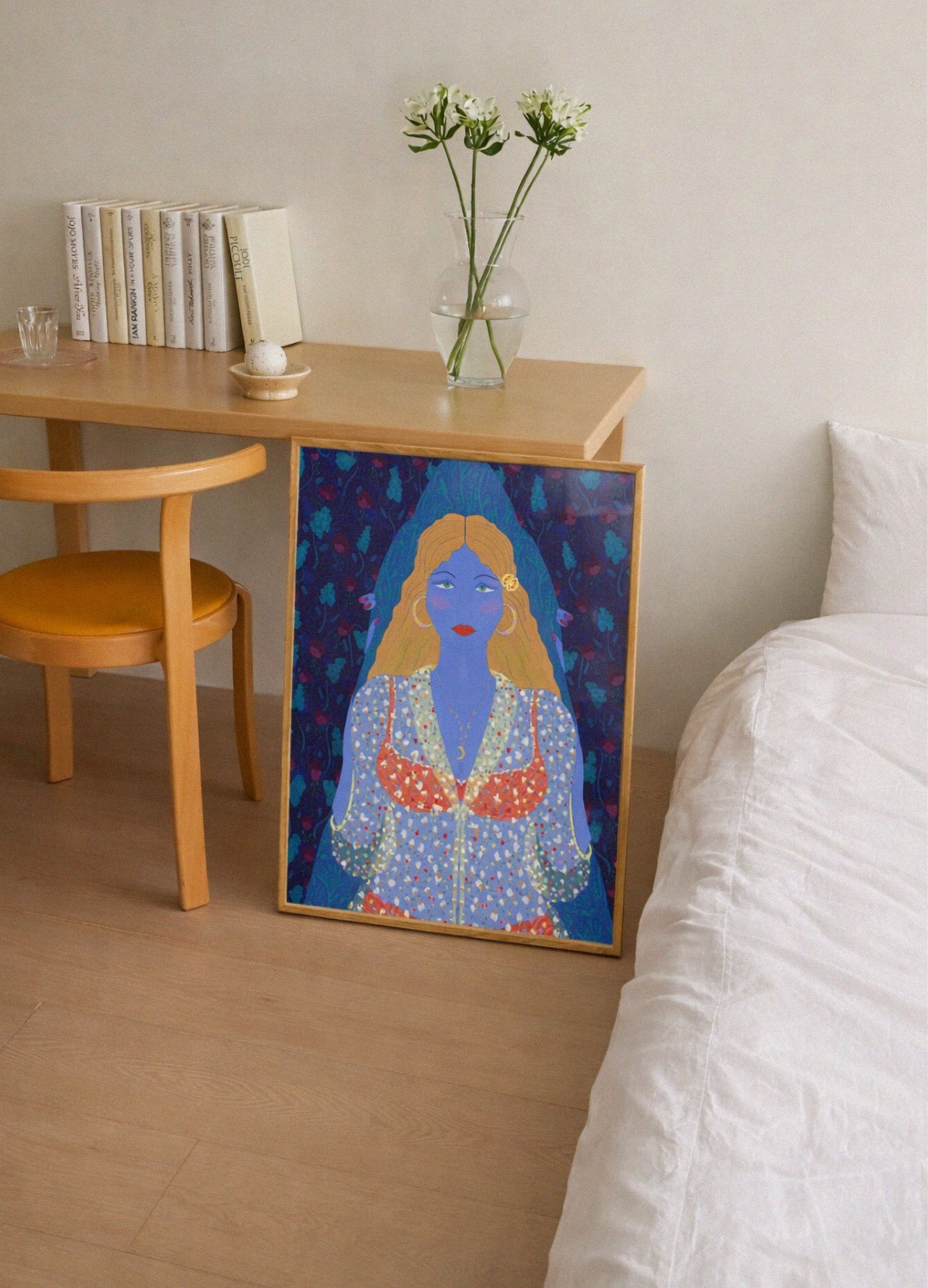 Framed artwork of a blue-skinned figure with long hair on a wooden side table next to a bed.