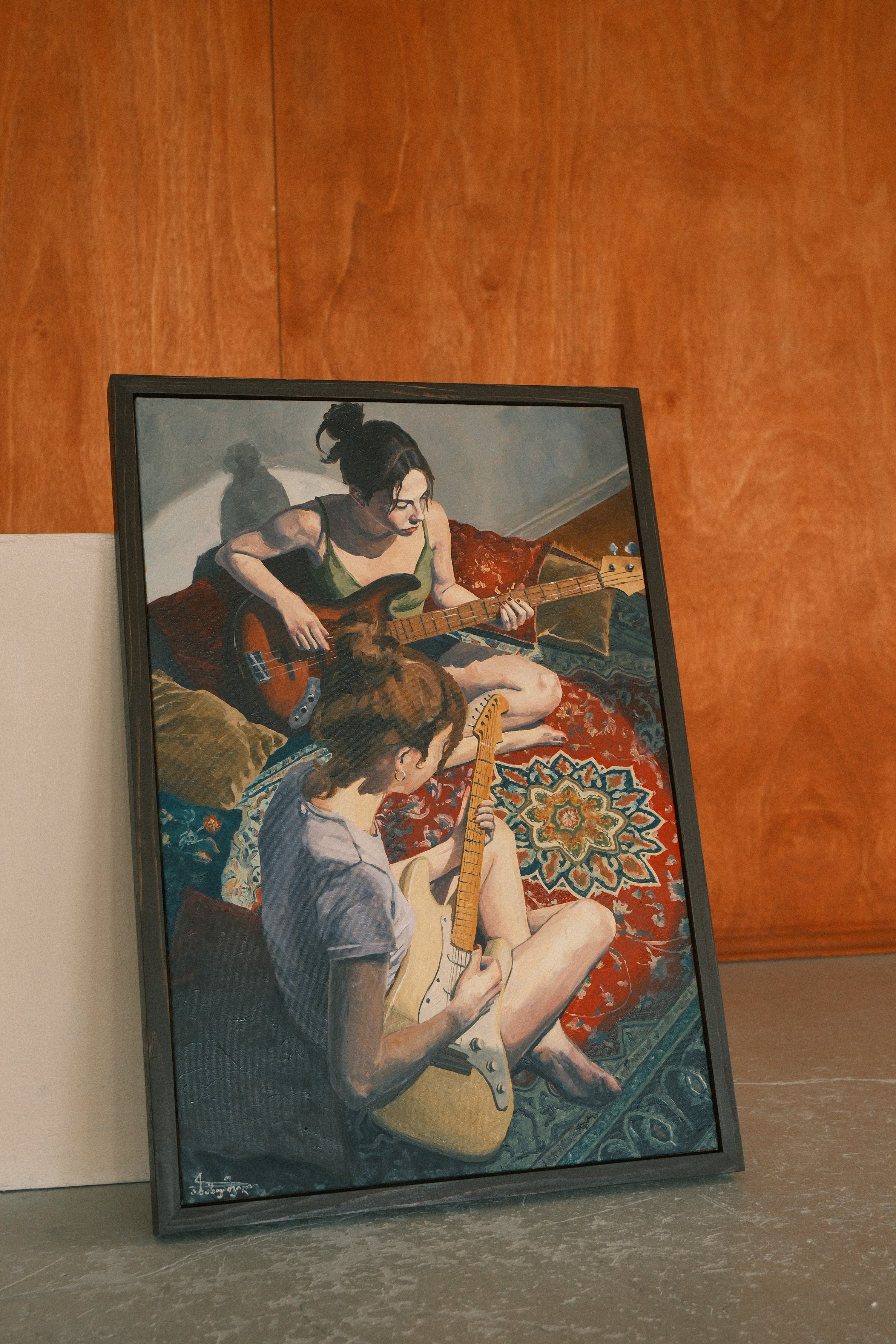 Framed artwork of two people playing guitars on a colorful rug against a wooden wall.