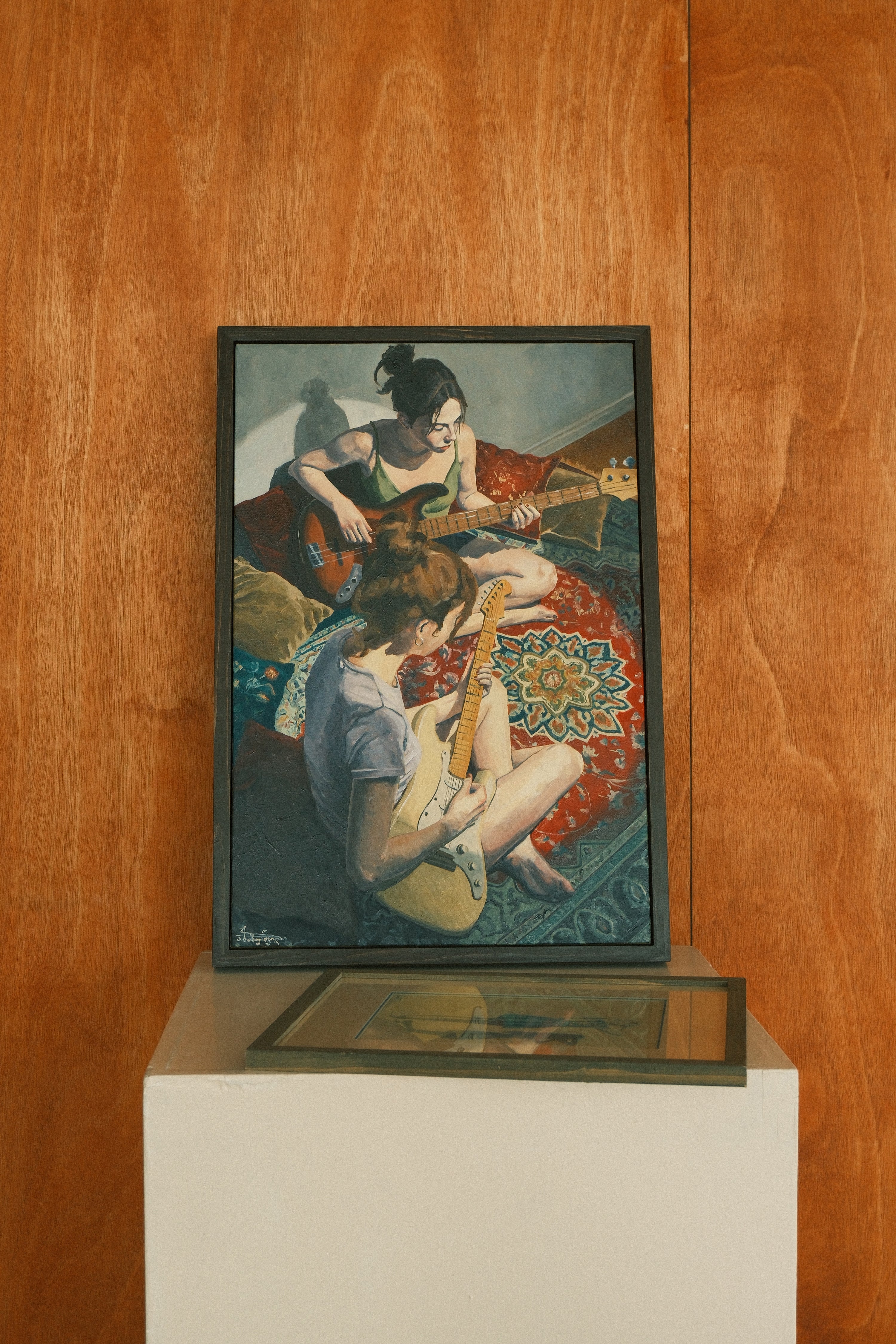 Framed artwork of two people playing guitar on a wooden wall.