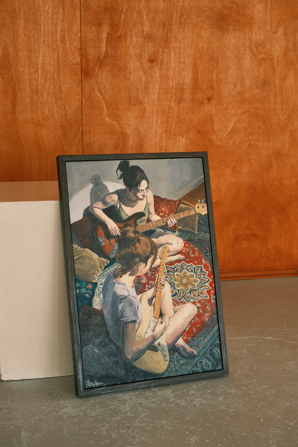 Framed artwork of two people playing guitar on a rug against a wooden wall.