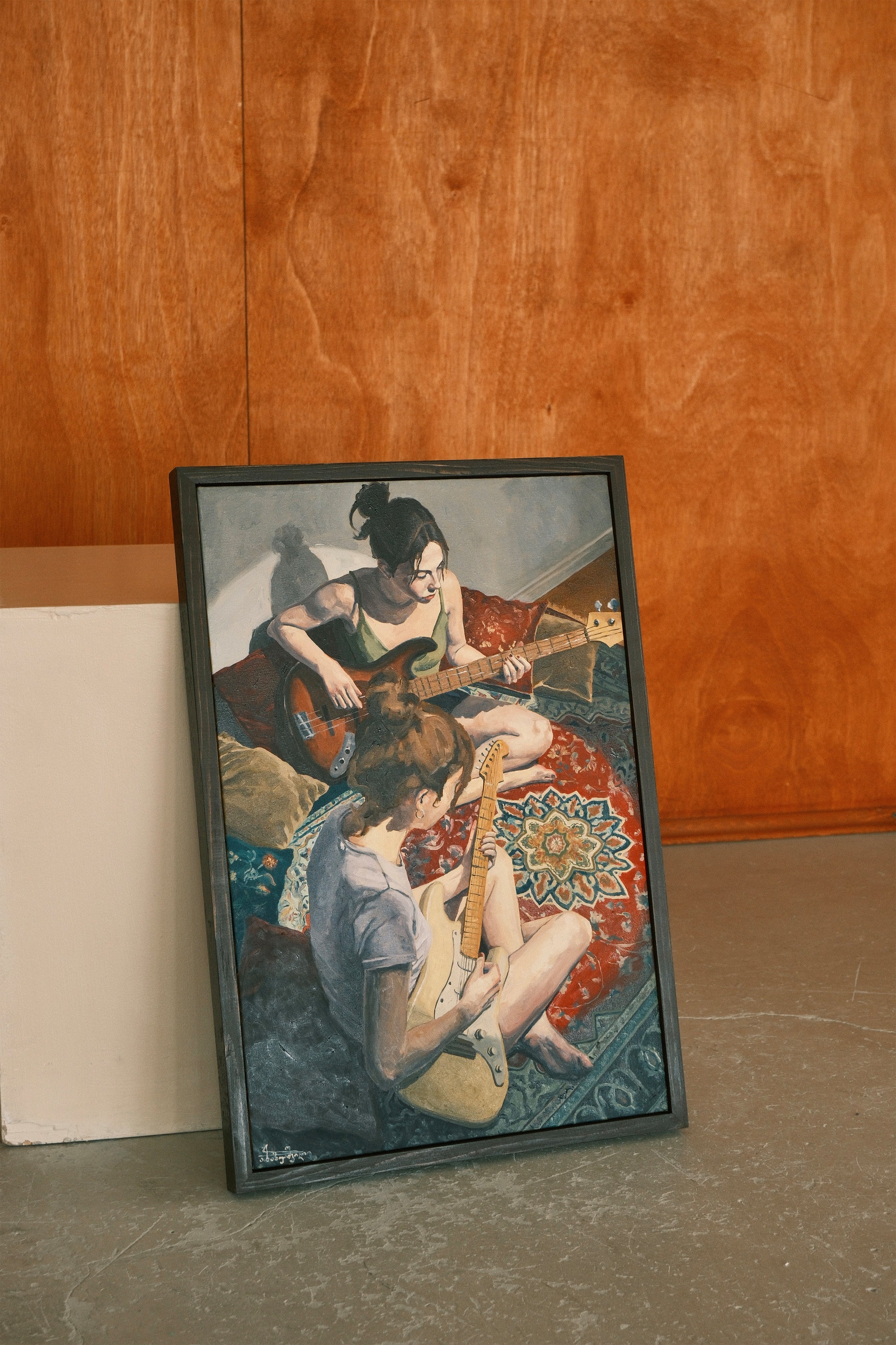 Framed artwork of two people playing guitar on a rug against a wooden wall.