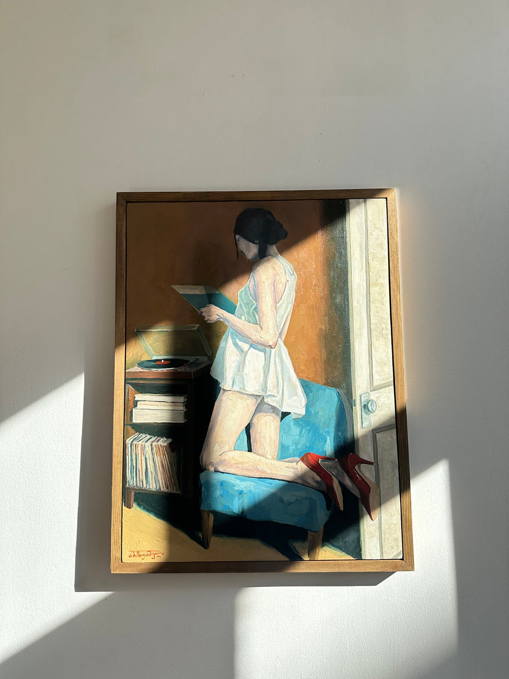 Framed artwork of a person sitting on a couch with books, on a light gray wall. DAE