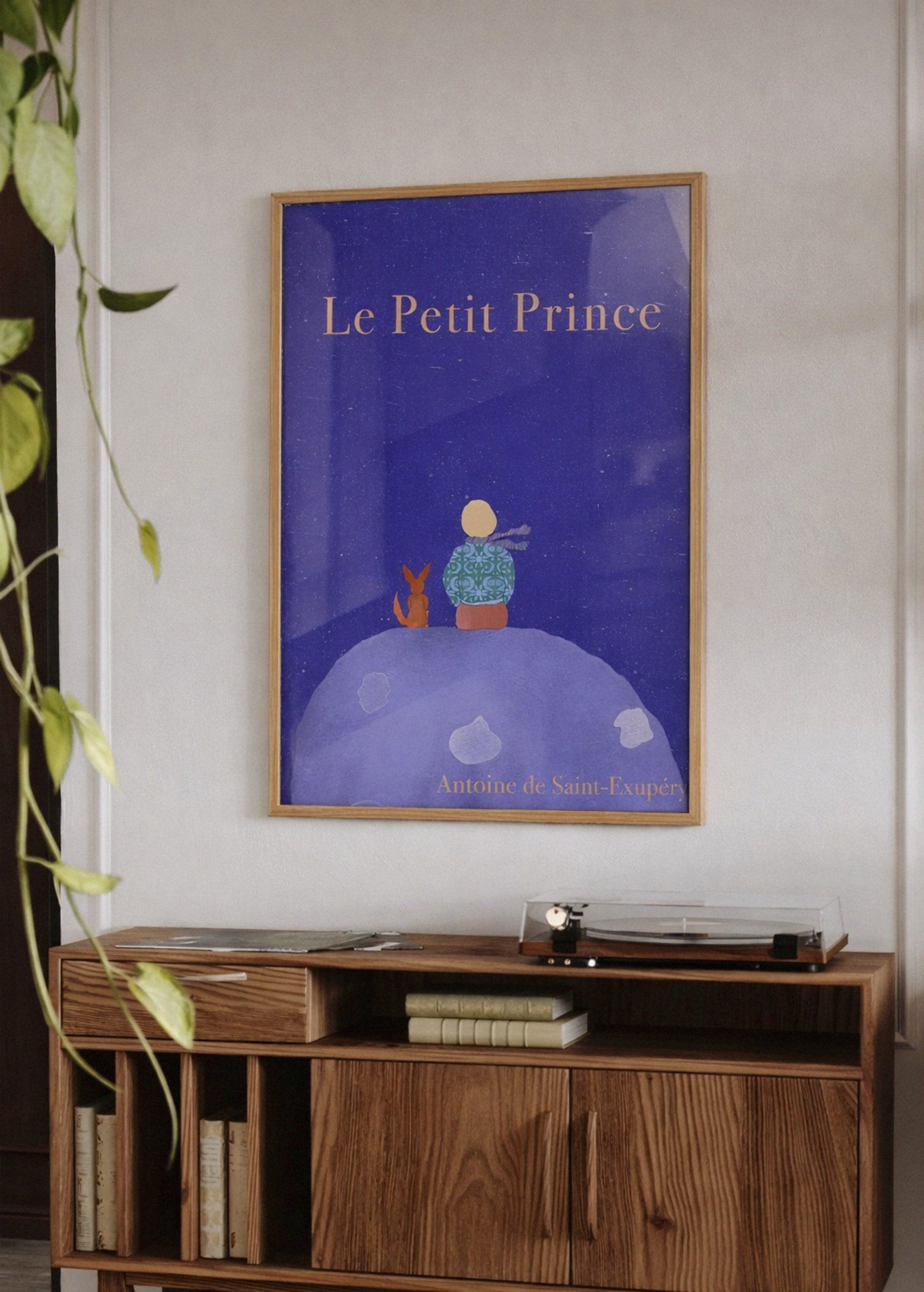 Framed 'Le Petit Prince' poster on a wall above a wooden cabinet.