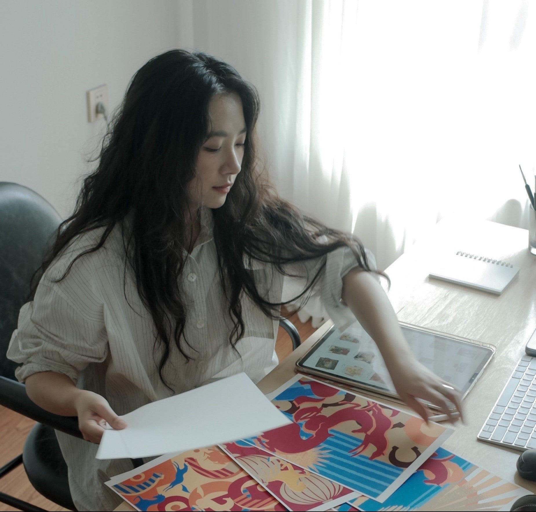 Woman sitting at a desk with colorful paper and a laptop in a bright room.
