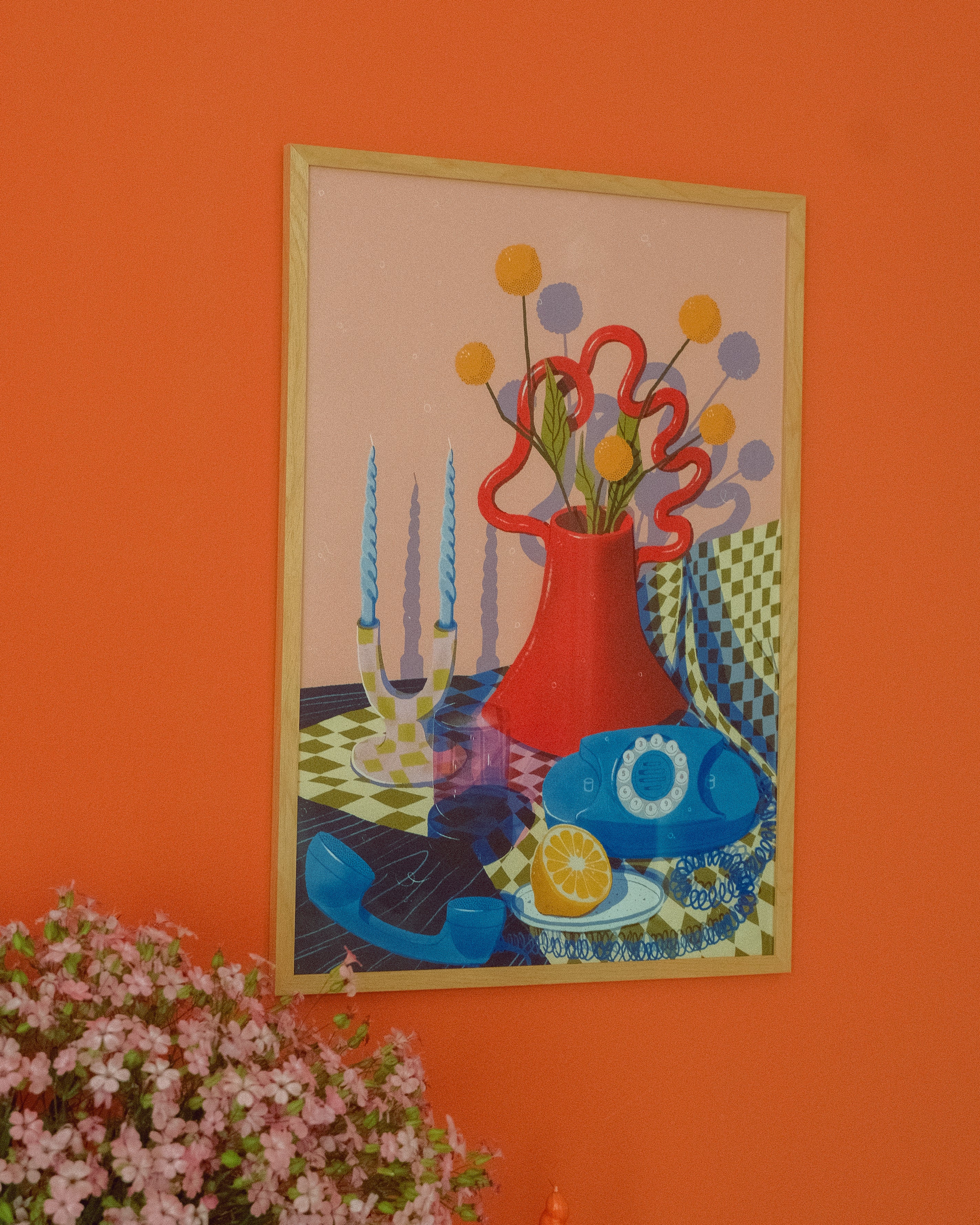 Framed artwork with a colorful still life scene on an orange wall.