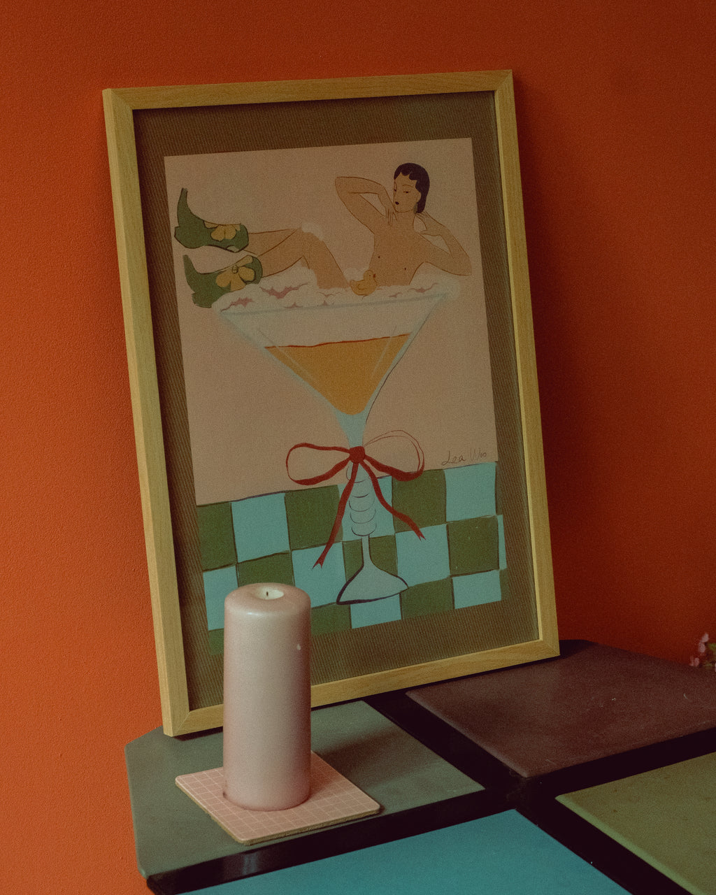 Framed artwork of a woman in a martini glass with a candle on a coaster below.
