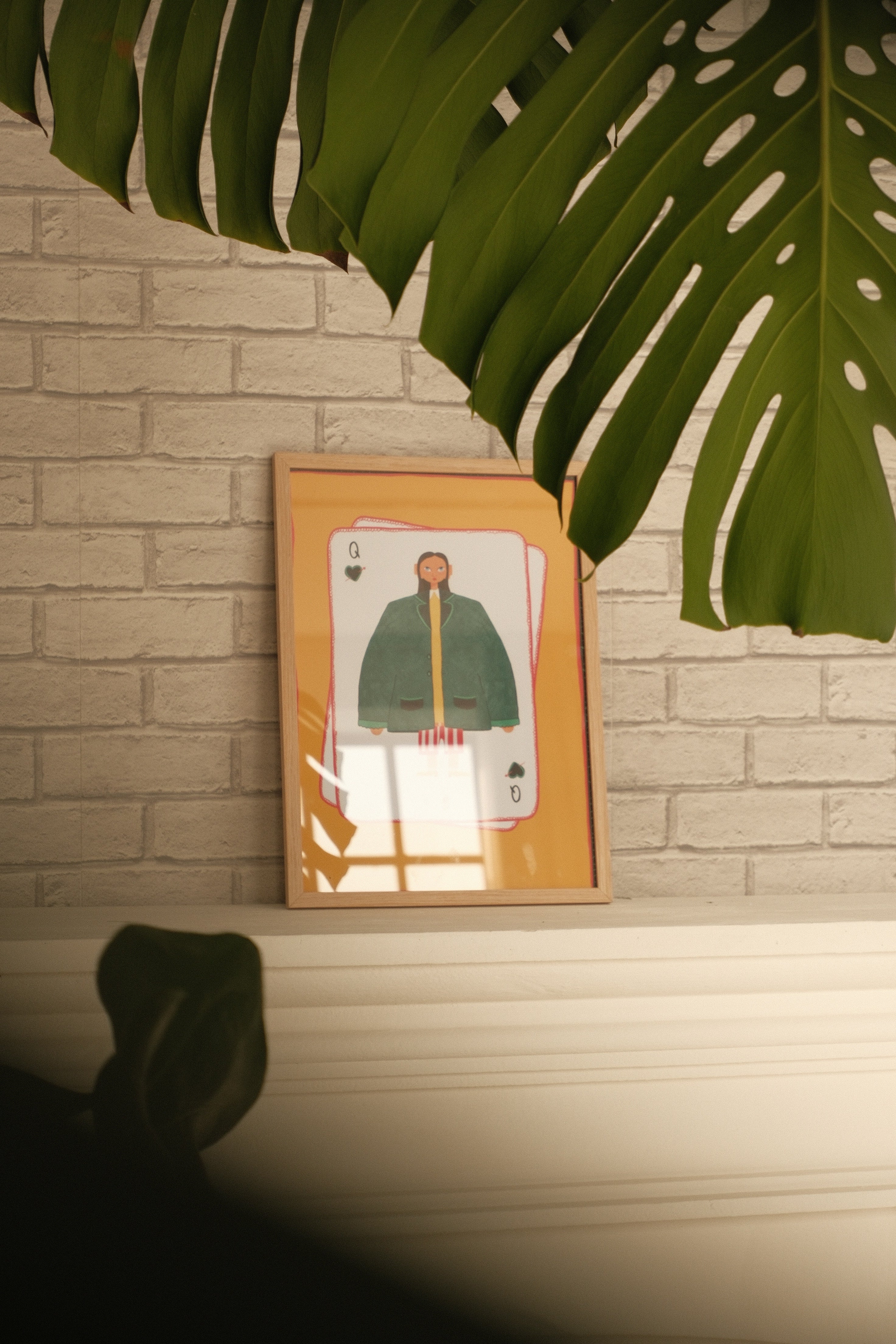 Framed artwork of a person in a green outfit on a textured wall with plant leaves.