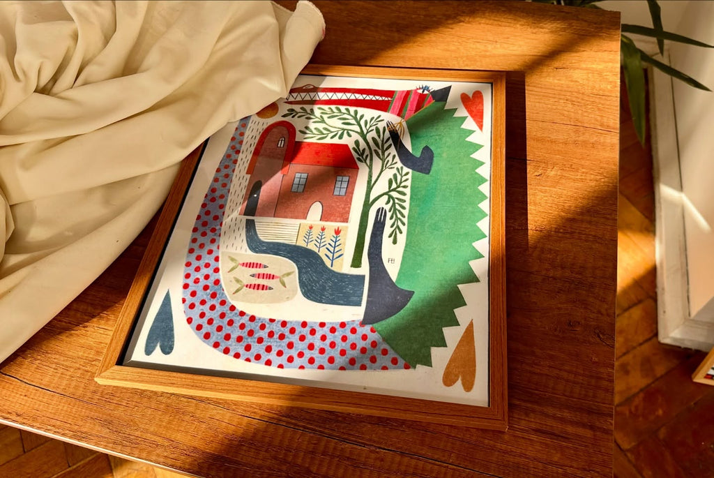 Framed artwork with a colorful design of houses and trees on a wooden surface.