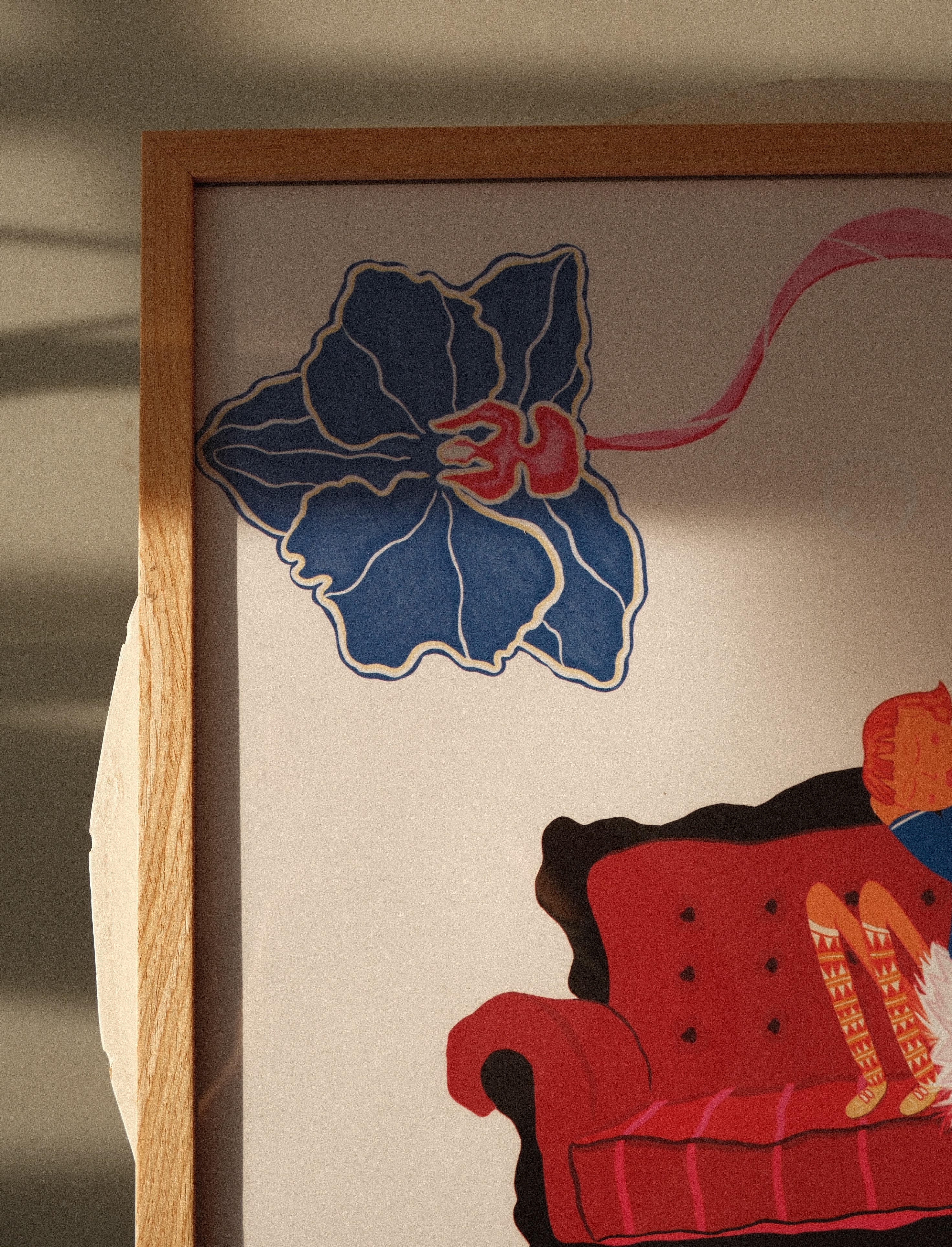 Framed artwork with a blue flower and red couch on a neutral background