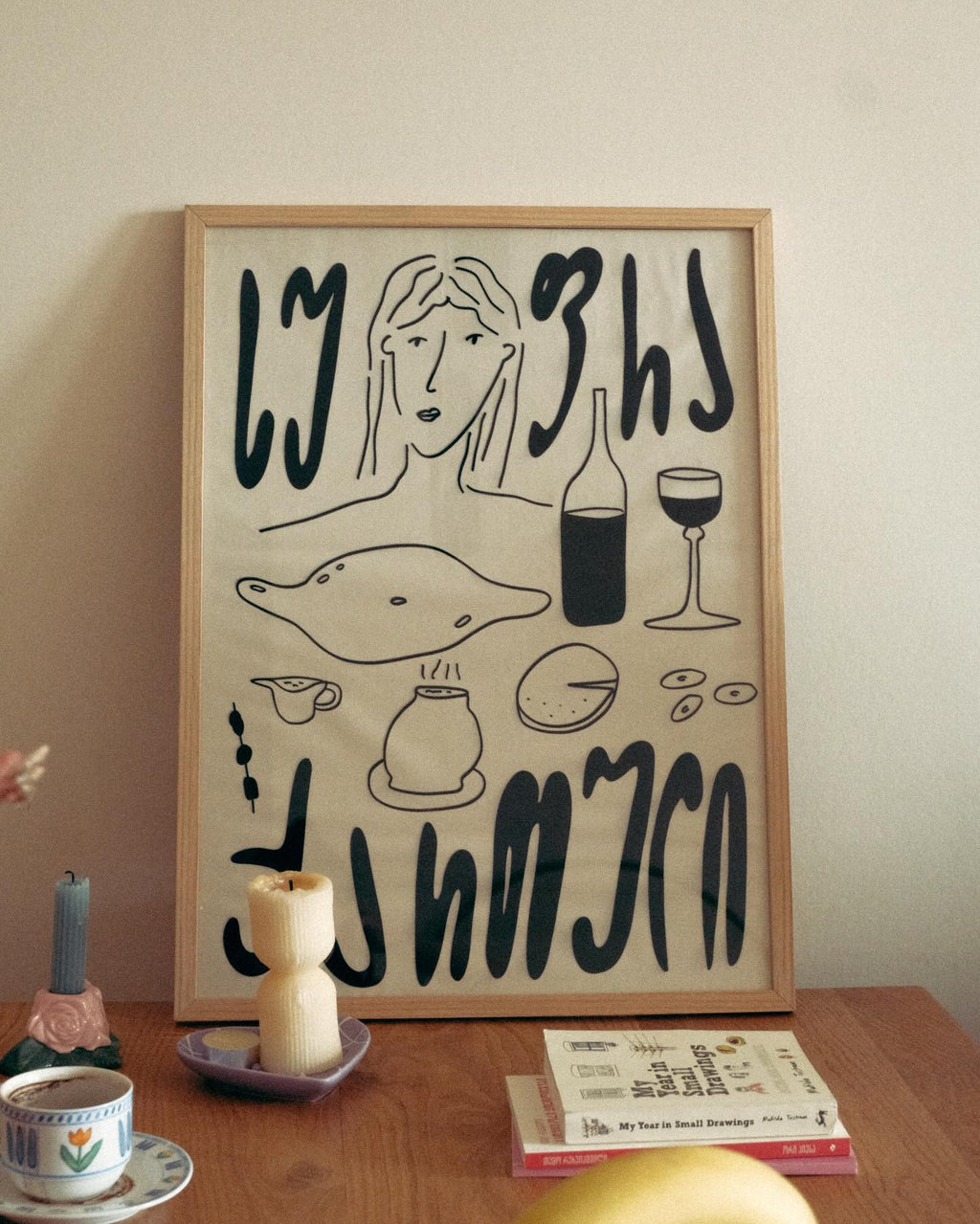 Framed artwork with black line drawings and text on a beige wall above a wooden table.