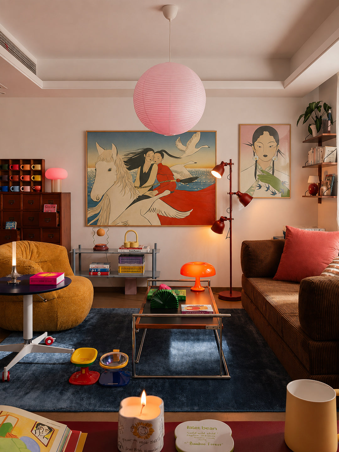 A cozy, stylishly decorated living room featuring a large pink paper lantern hanging from the ceiling, a colorful abstract painting of a horse and rider on the wall, a brown sofa with a coral pillow, and a blue rug.