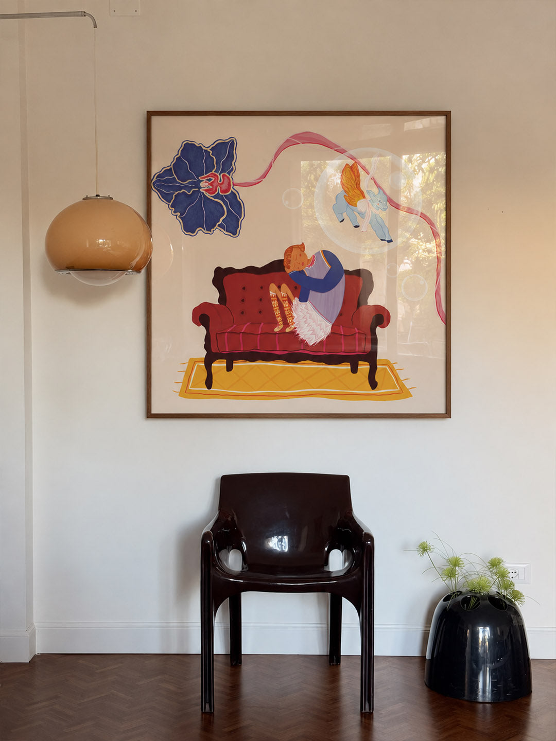 A framed art print featuring a whimsical illustration of a person sitting on a red sofa with blue and yellow abstract shapes, displayed on a white wall above a dark brown chair in a styled interior. Wall art by DAE