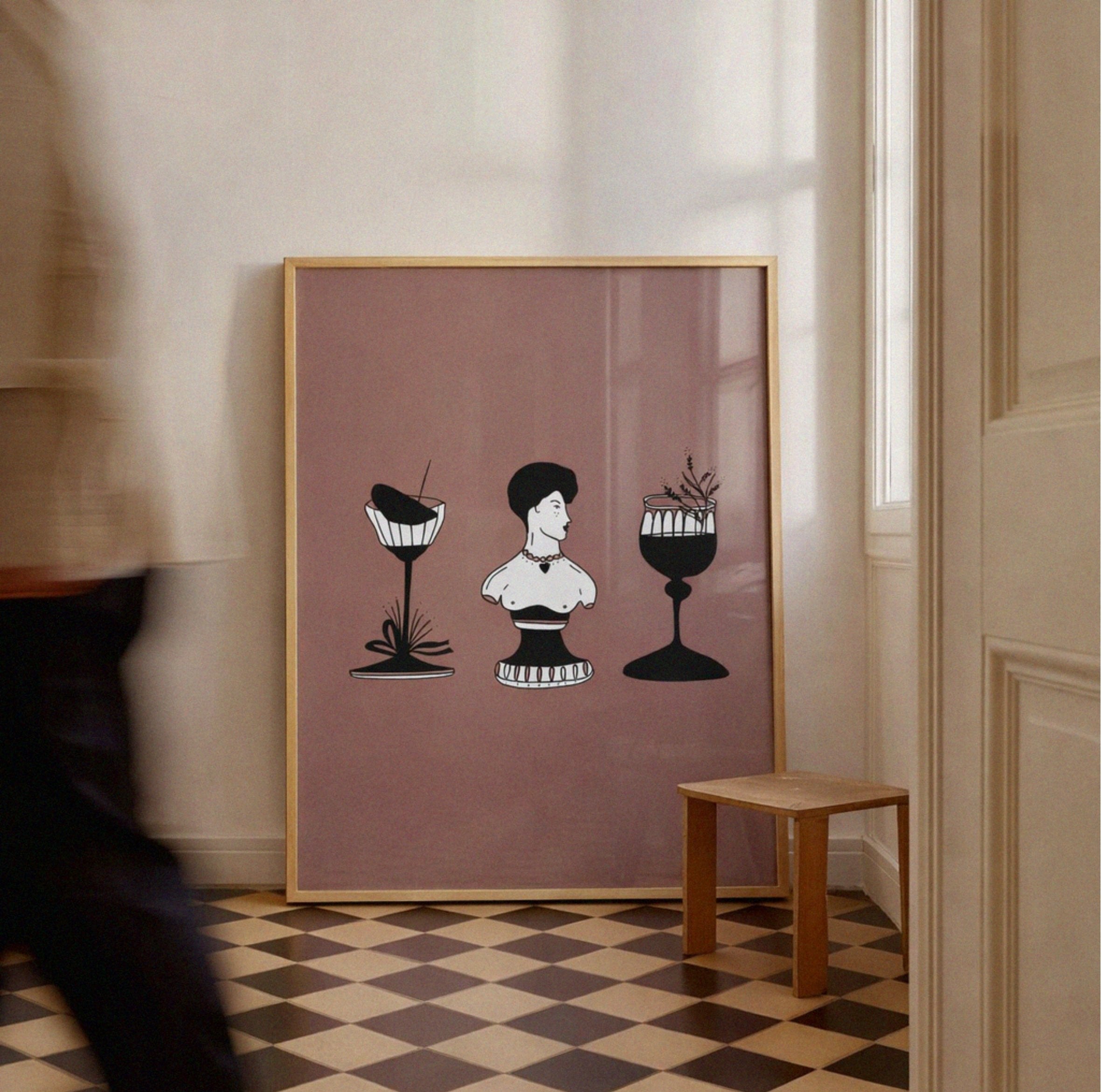 Framed artwork with a stylized illustration of a woman and two cocktails on a checkered floor.