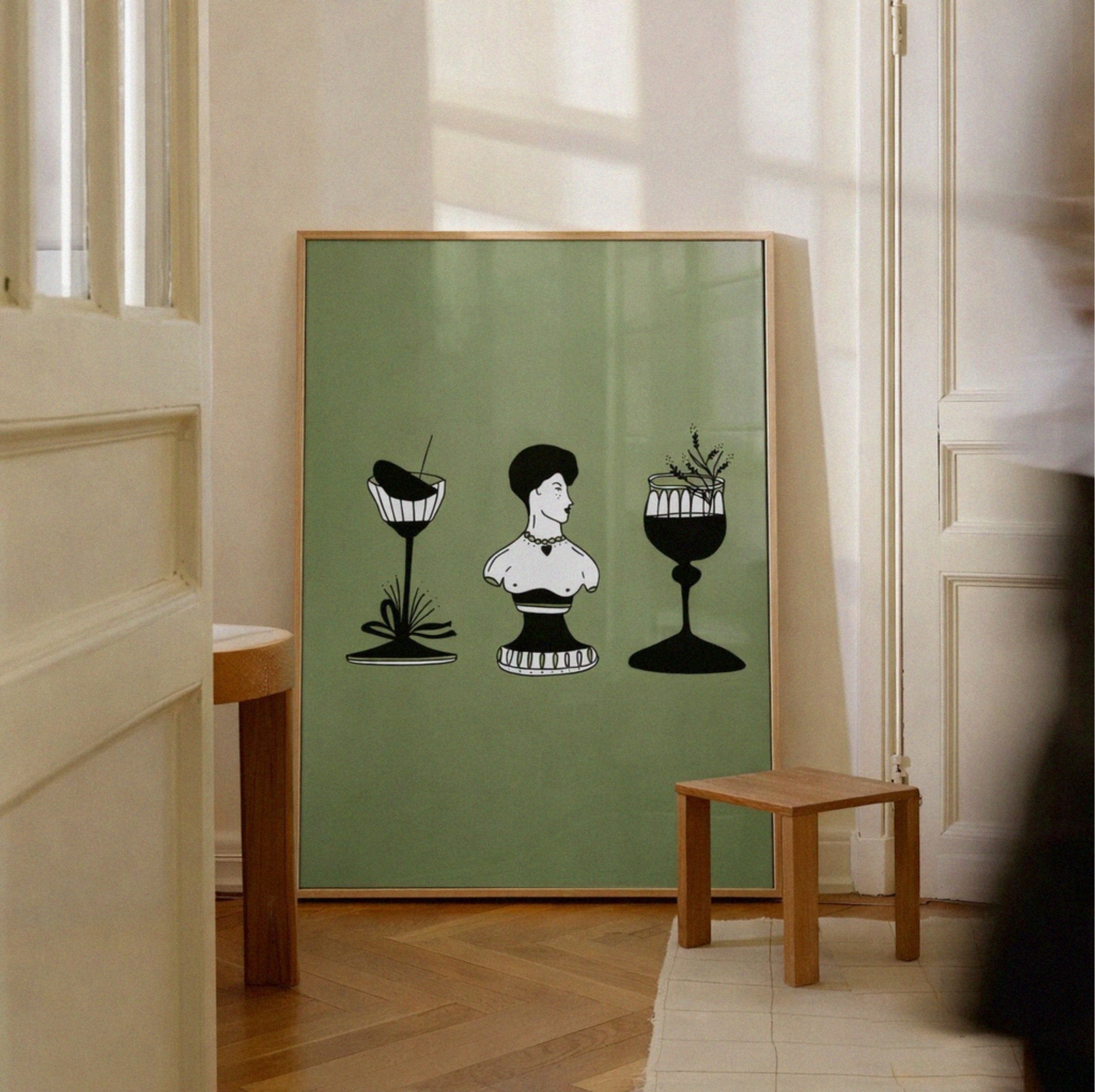 Framed artwork with black and white illustrations on a green background, displayed in a room with wooden floor and white walls.