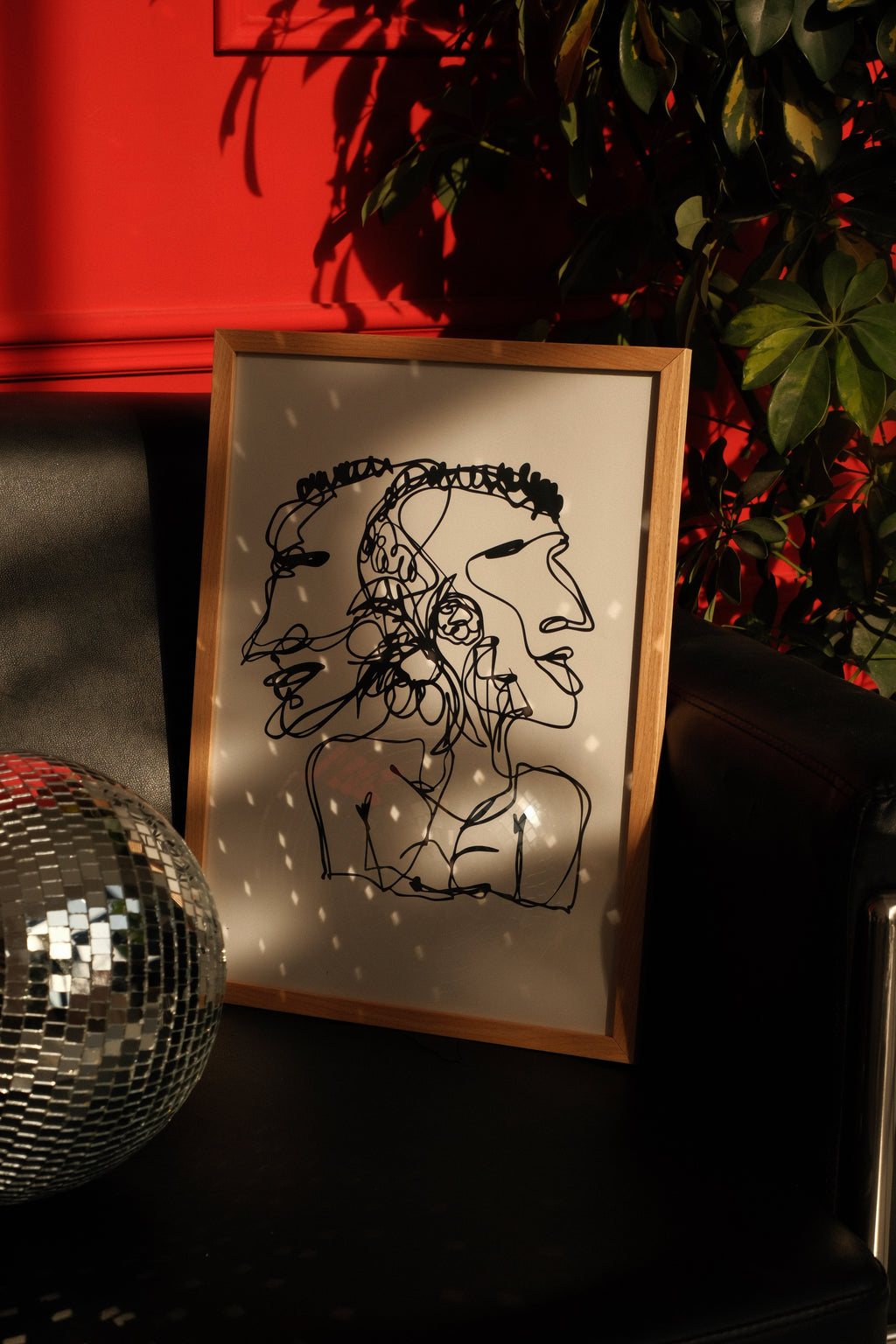 Framed line drawing of a person with a flower in their hair on a dark surface with a disco ball and red wall in the background.