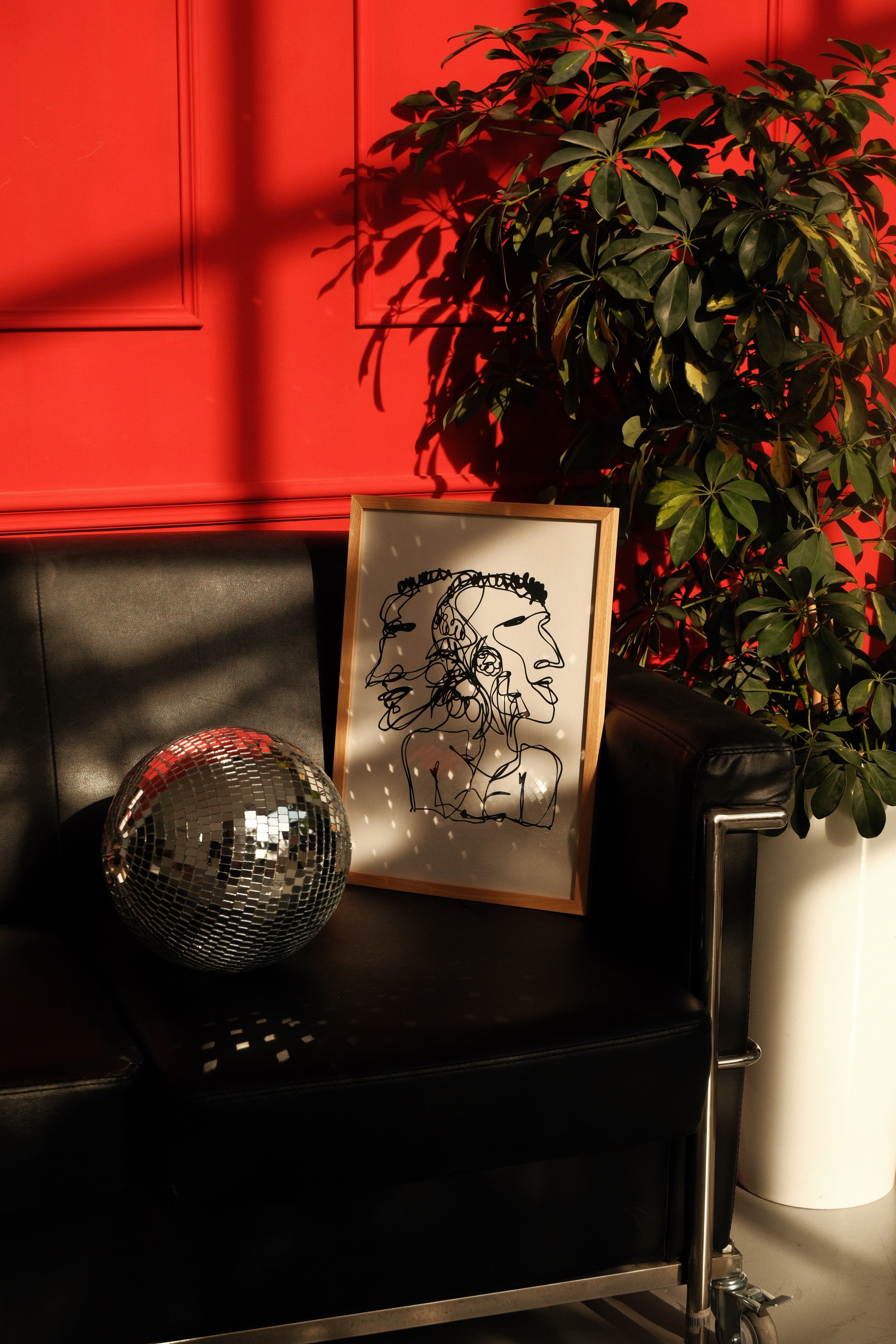 poster with face design on a black surface against a red wall with a plant.