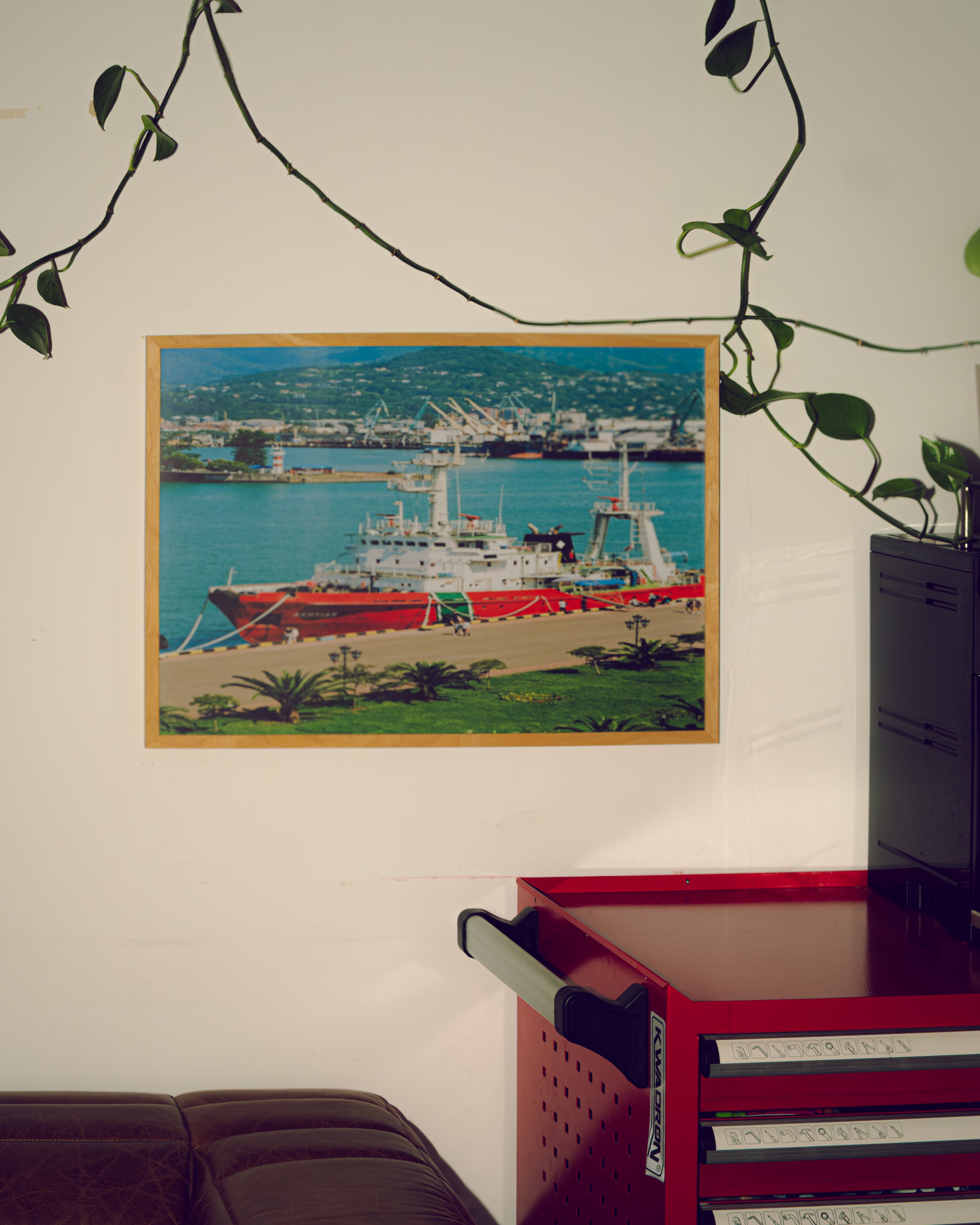 Framed artwork of a ship on a wall above a red toolbox.