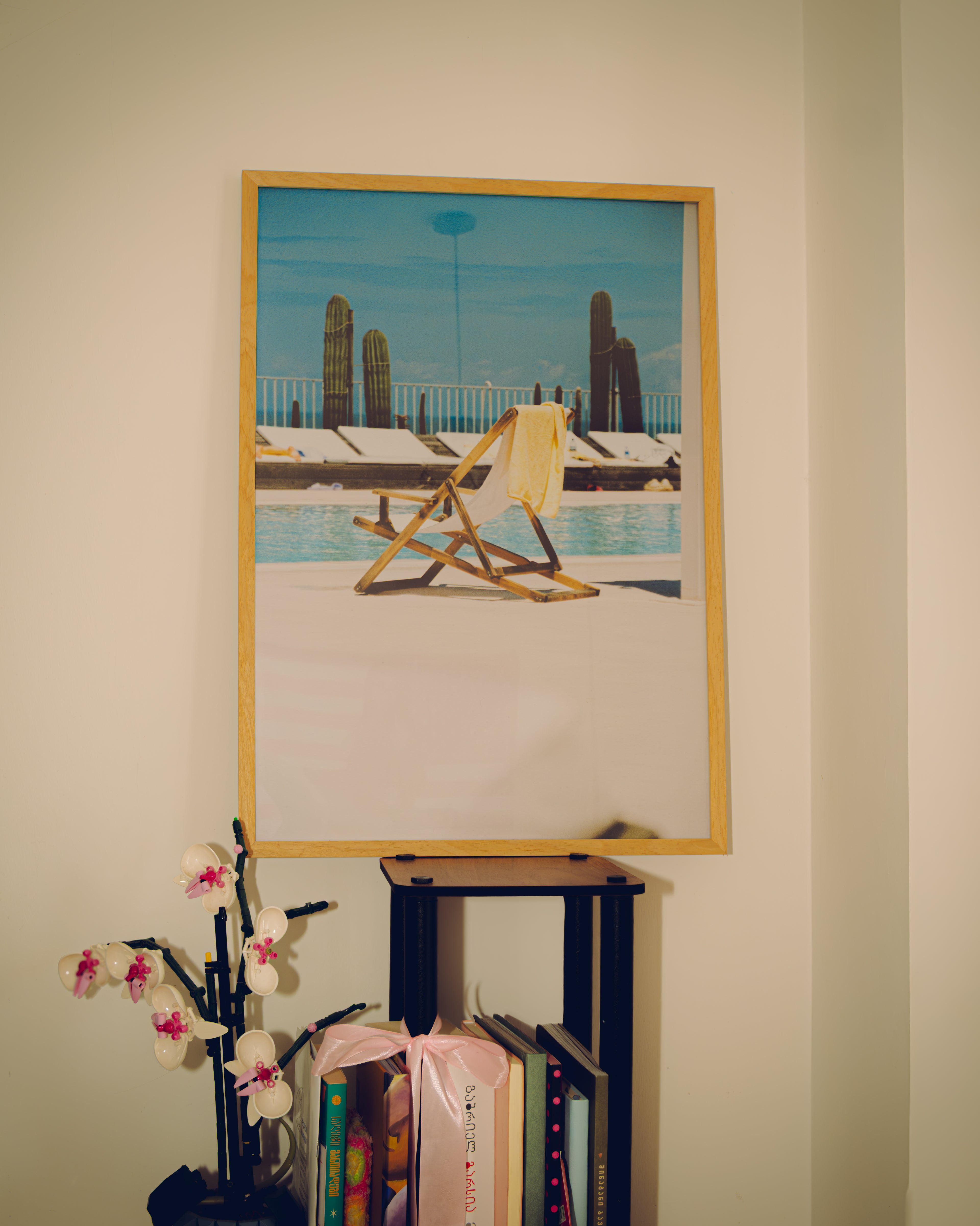 Framed artwork of a poolside scene with a yellow chair on a beige wall.