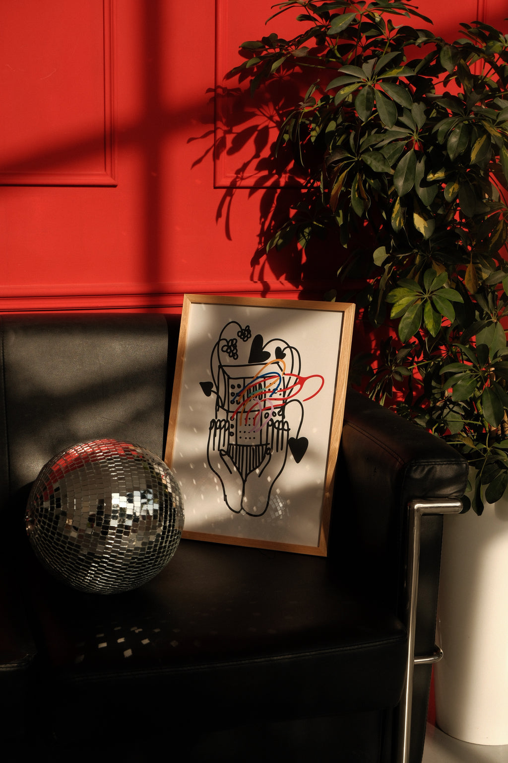 Decorative mirror ball and framed artwork on a black surface with a red wall and plant in the background.