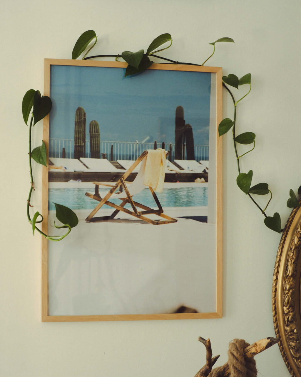 Framed picture of a beach scene with a chair and towel, surrounded by greenery on a light-colored wall.