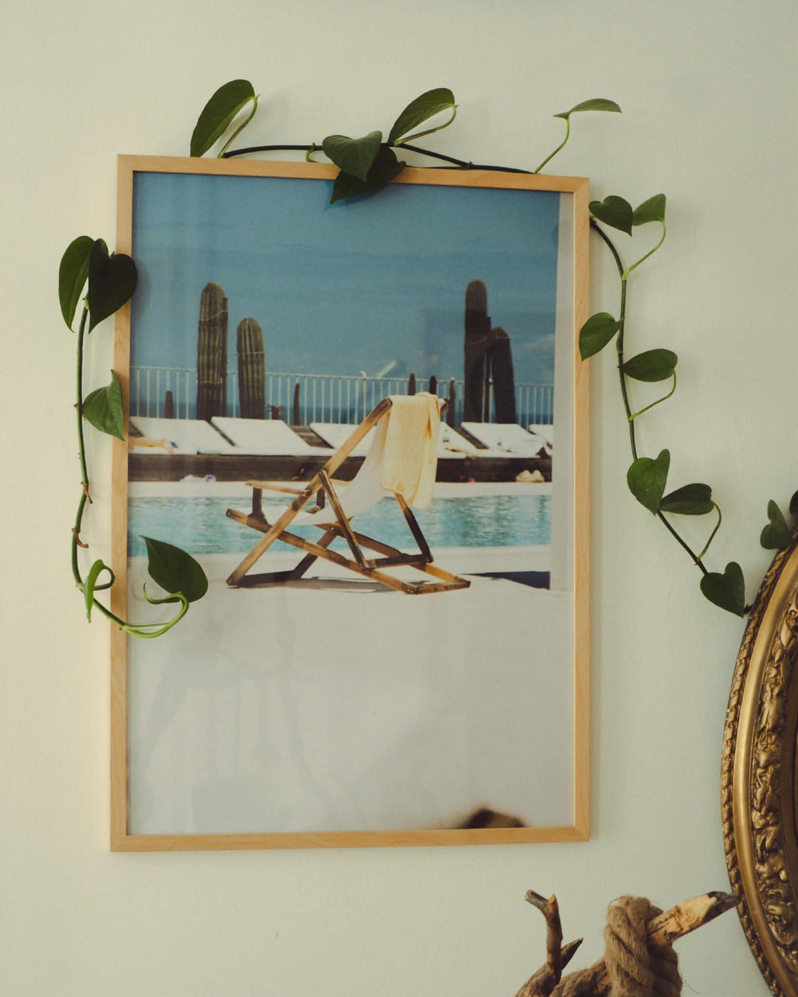 Framed picture of a beach scene with a chair and towel, surrounded by greenery on a light-colored wall.