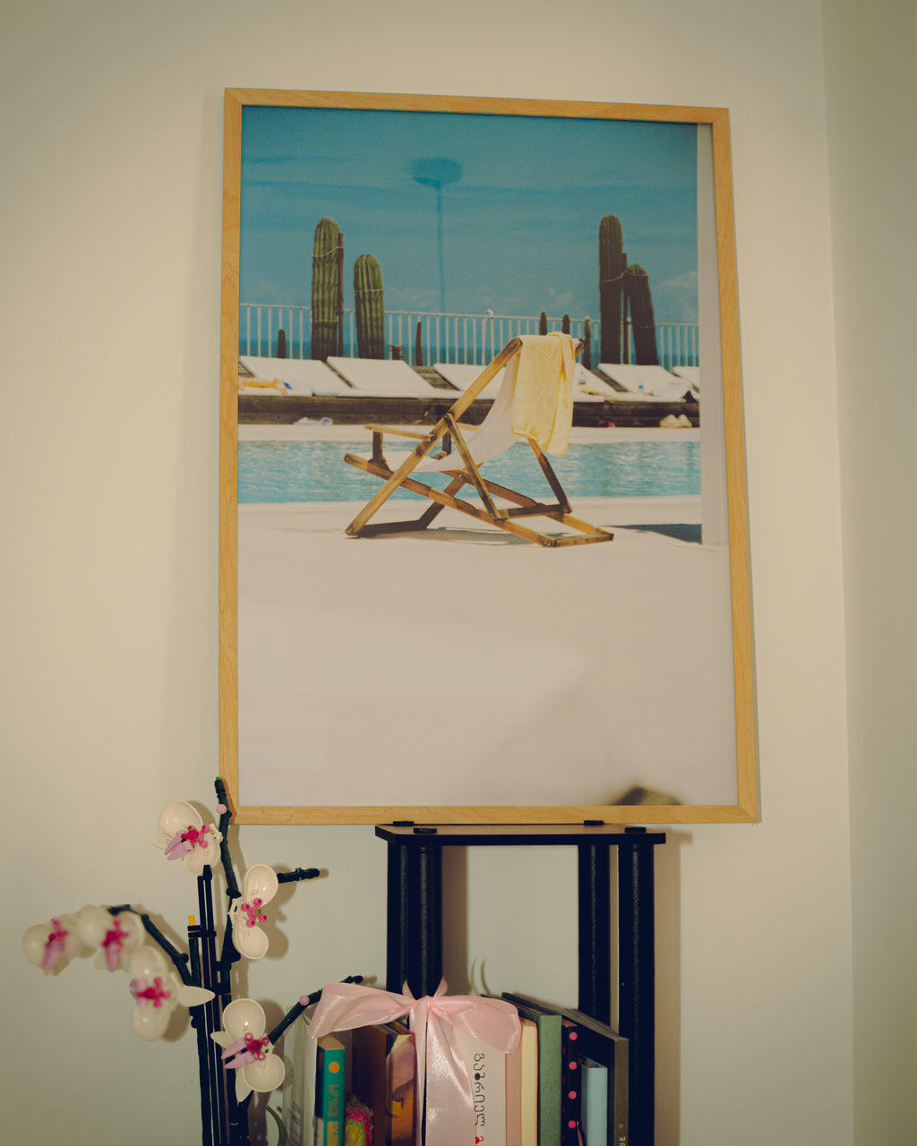 Framed artwork of a poolside scene with a chair and towel, displayed on a wall.