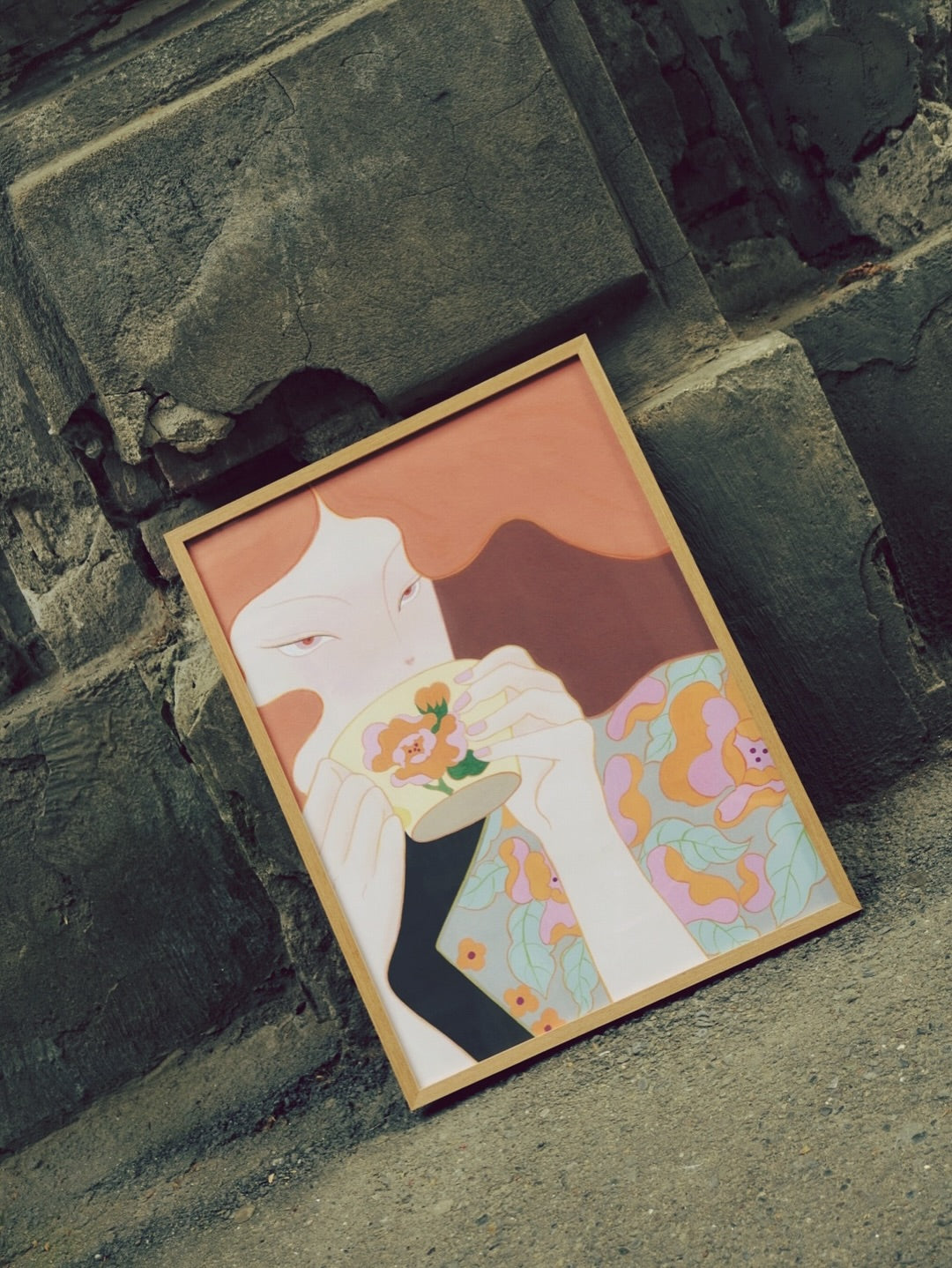 Framed artwork of a girl holding a tea and wearing flower printed dress on a stone wall background