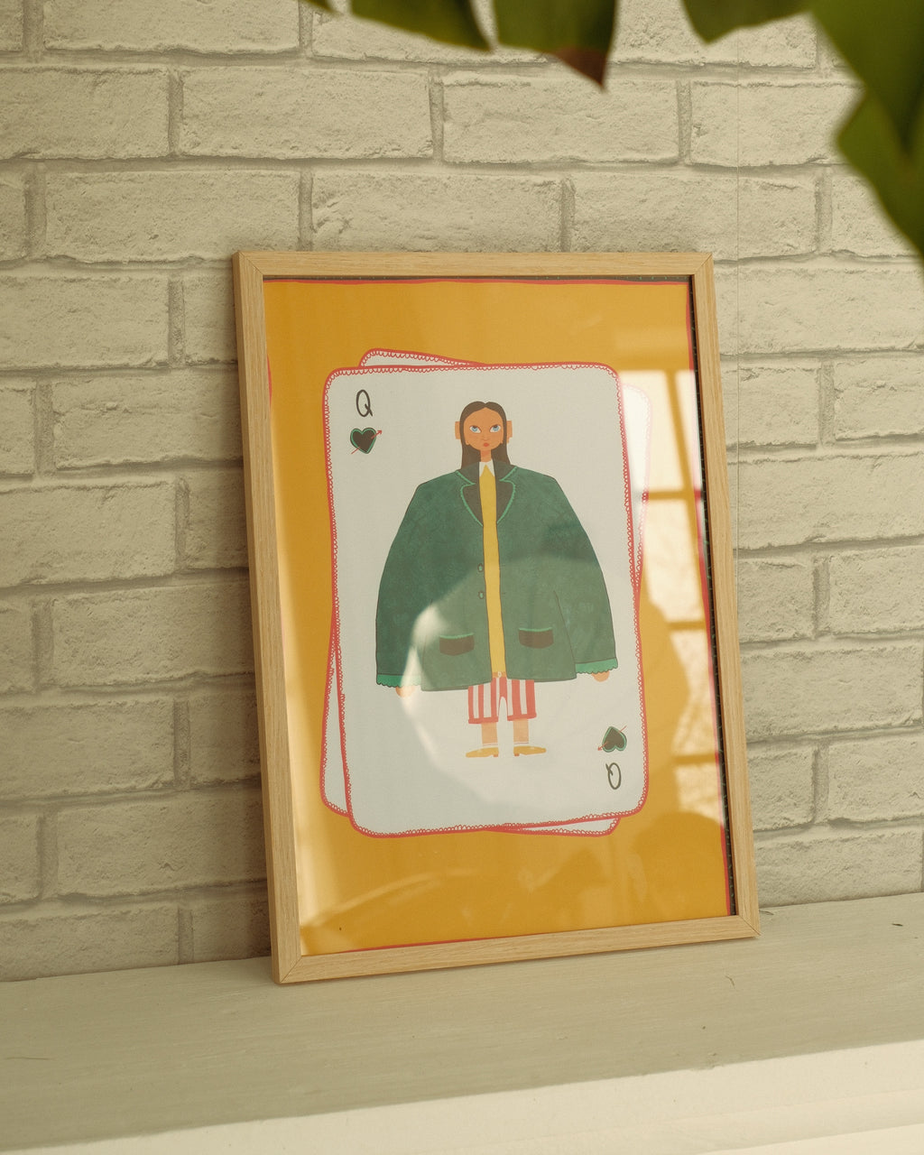 Framed artwork of a card with a person wearing a green coat against a brick wall.