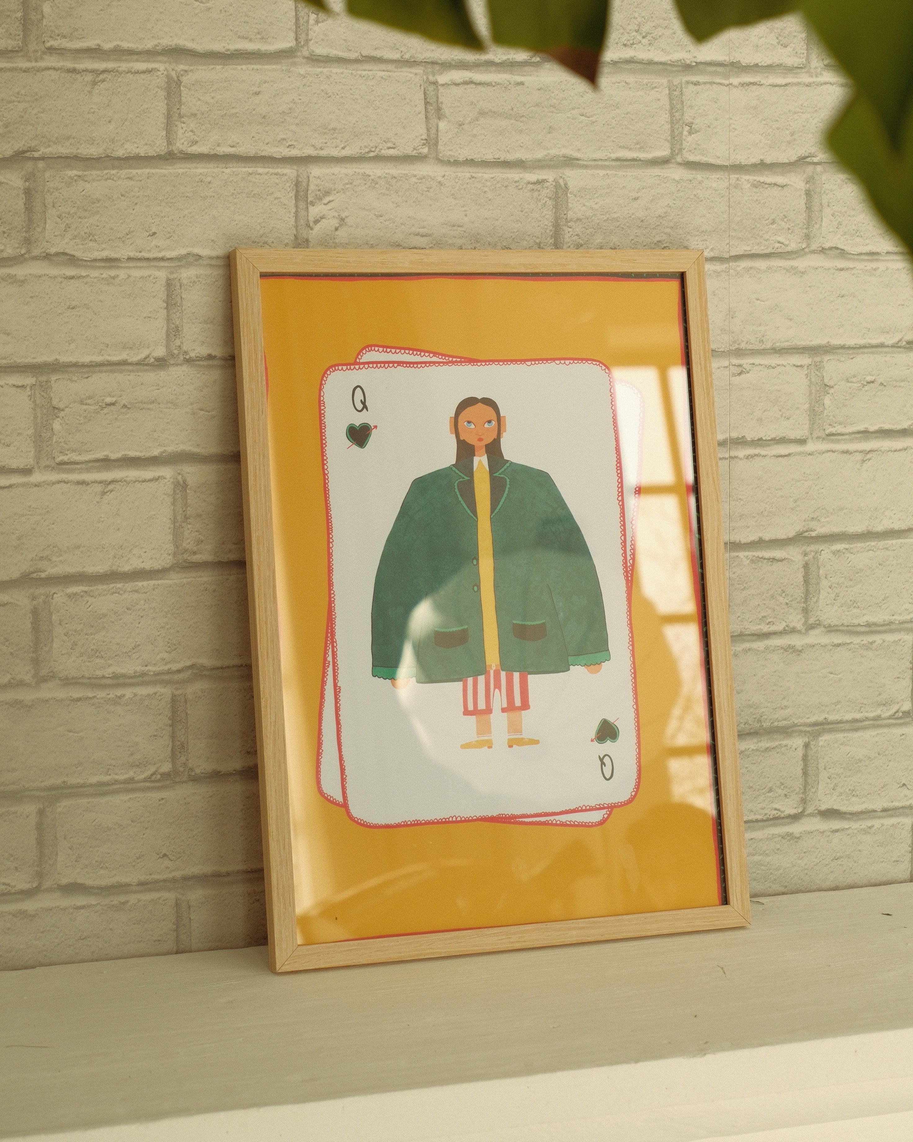 Framed artwork of a card with a person wearing a green coat against a brick wall.