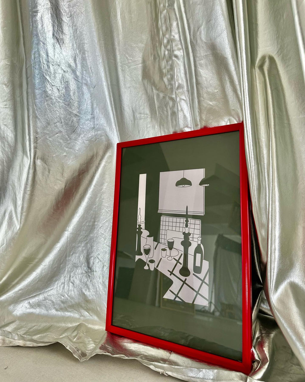 A poster depicting a stylized dining room setting with a red frame, displayed against a silver fabric background.