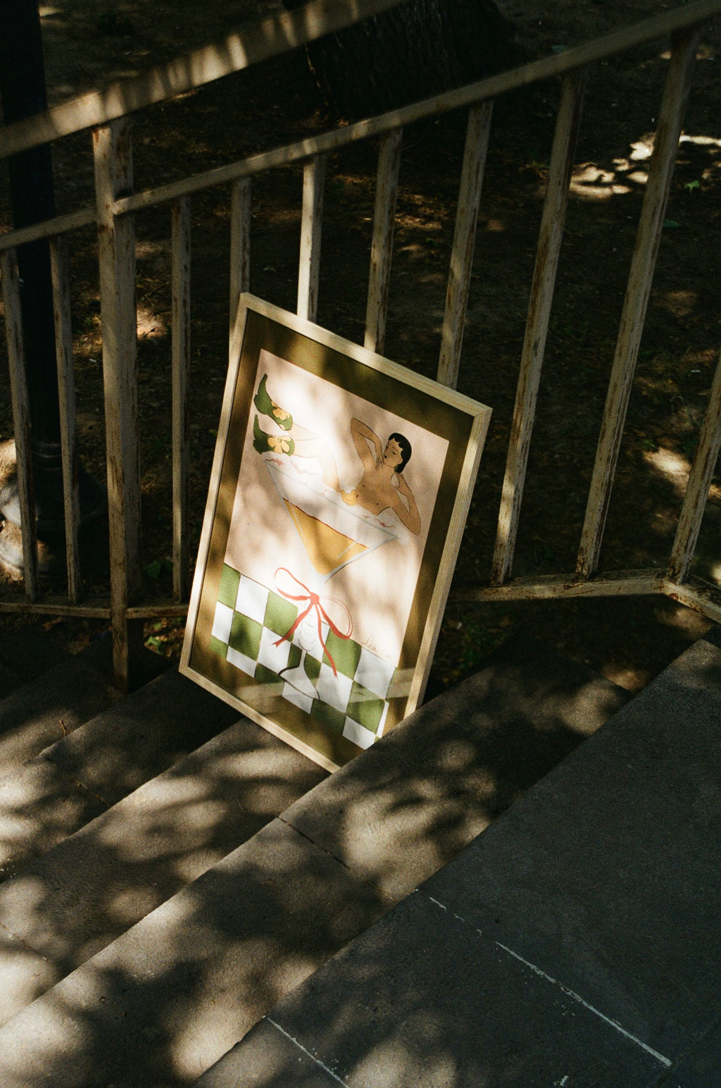 Framed picture leaning against a metal railing on a sunlit path