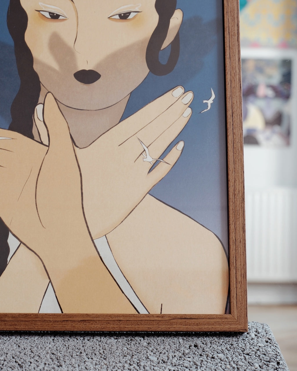 Framed artwork of a woman with a hand near her face, set against a blue background.