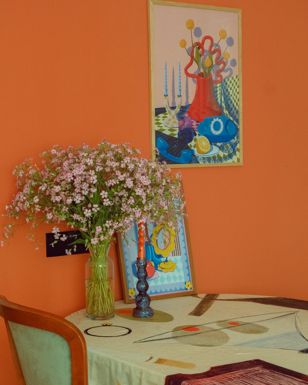Vase of flowers on a table with colorful abstract paintings on an orange wall.