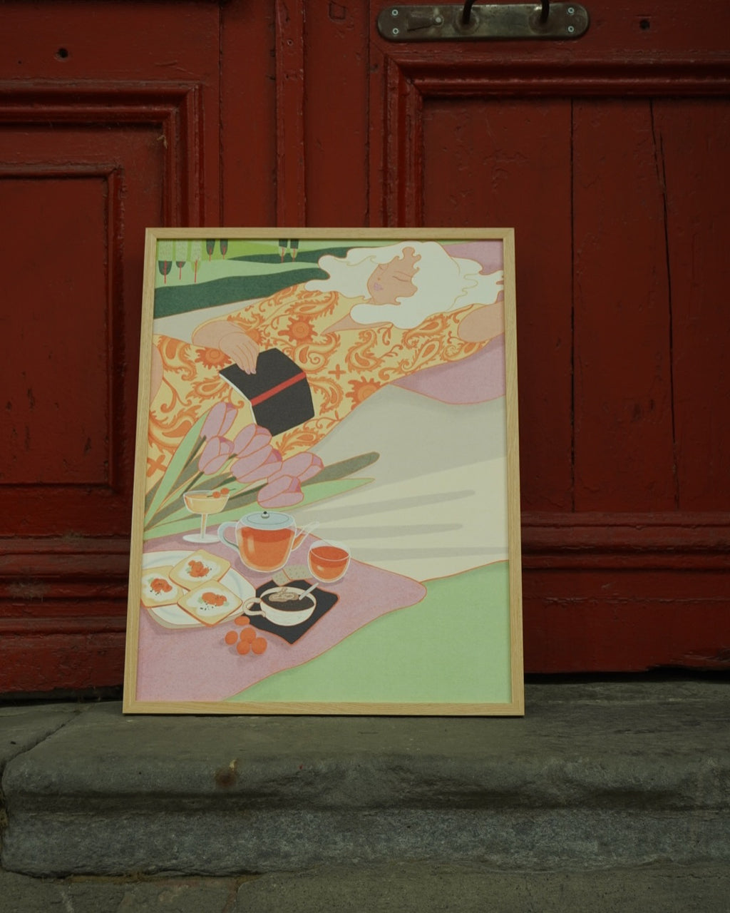 Framed “Savoring the Sunshine” poster held in front of a red wooden wall, showing a soft, dreamy illustration.
