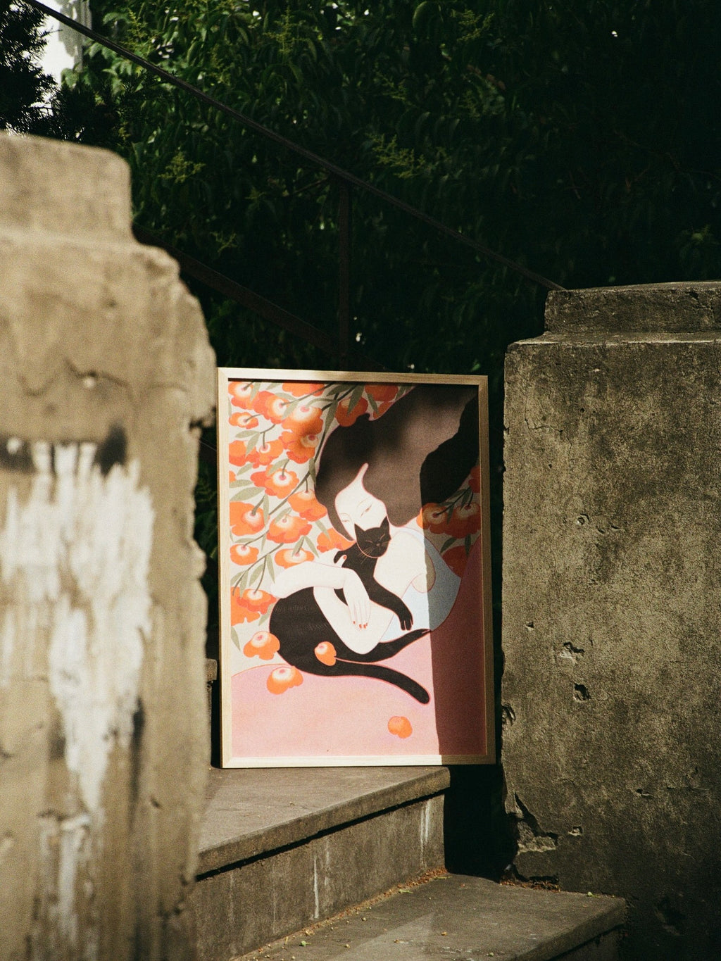 Framed poster of a woman with flowers on the back and a holding cat. Poster is standing on the stairs, tree on the back