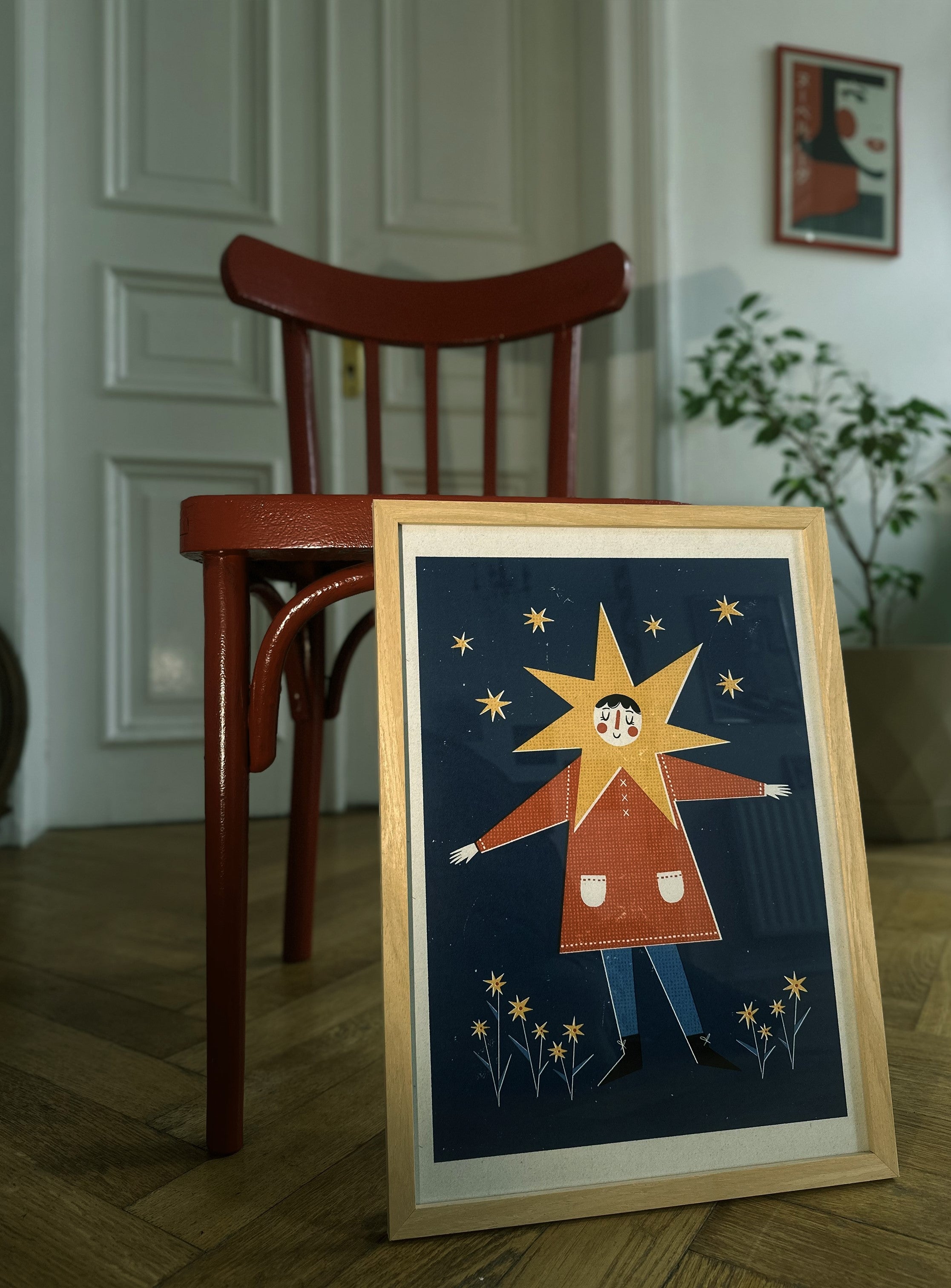 A framed poster featuring a colorful illustration of a character reaching towards a star, displayed on a wall against a neutral background.