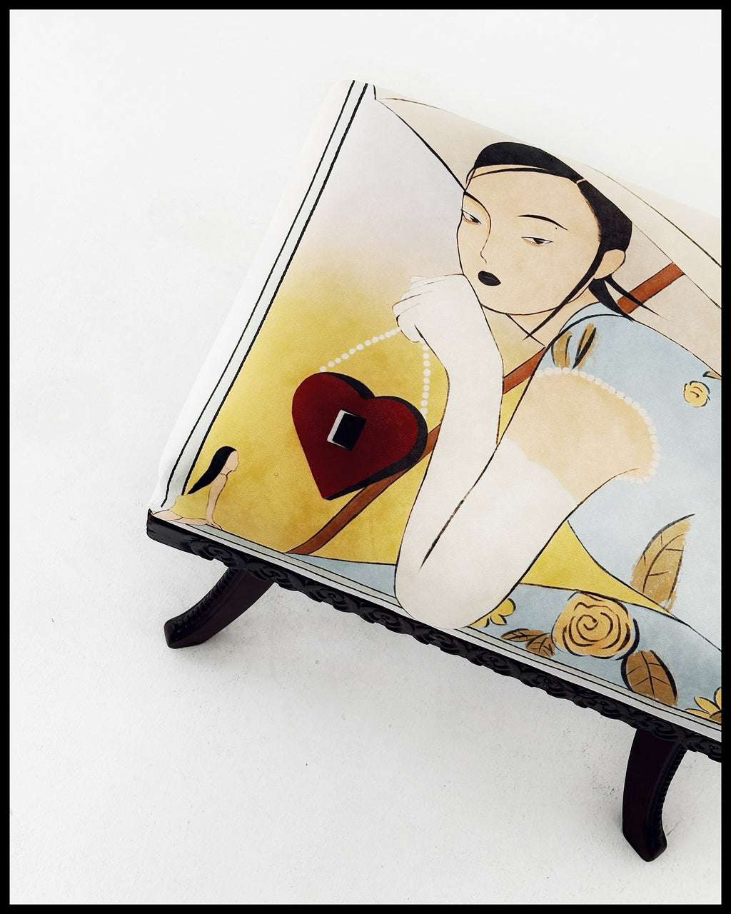 A decorative pouf featuring fabric printed with an illustration by Lea Woo, depicting a woman in a yellow dress with a red heart.
